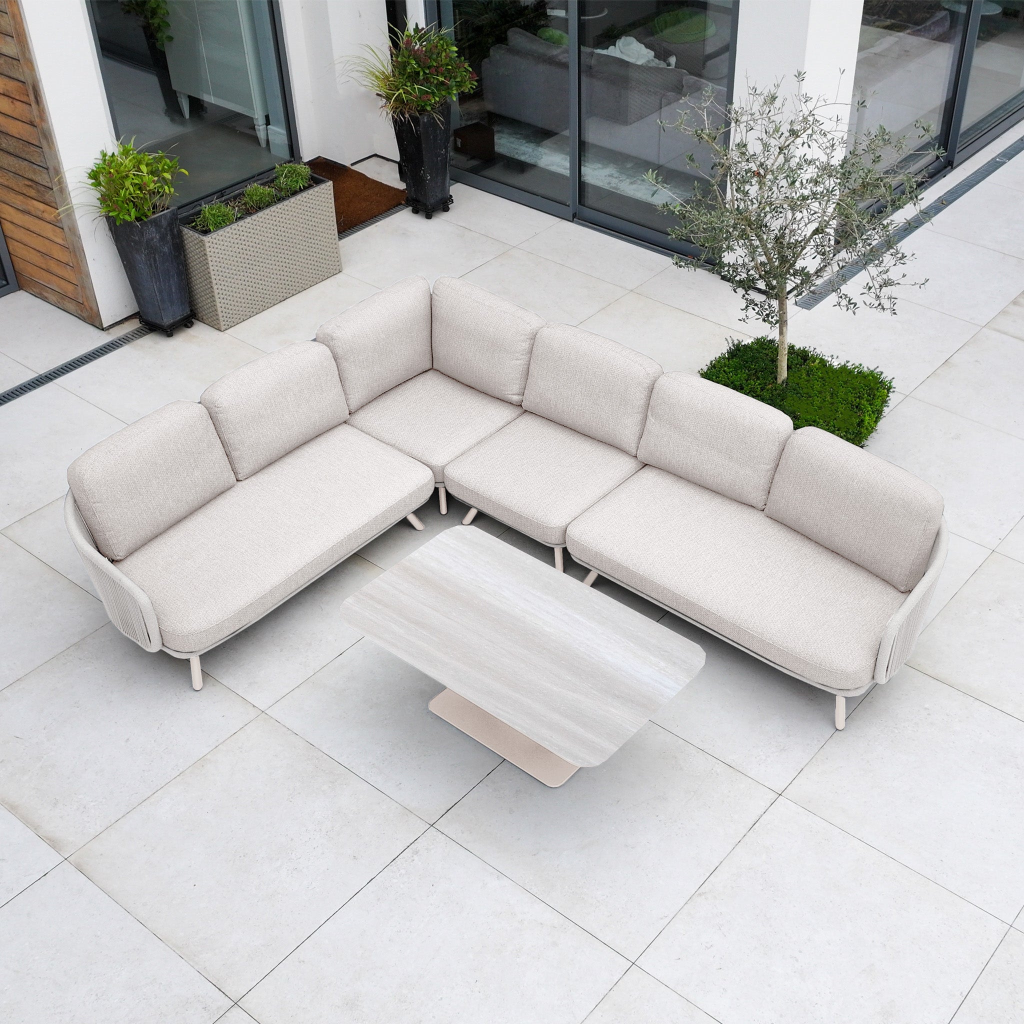The Dekota Large Corner Sofa Dining Set with Altura Rising Table in Fawn sits on a modern tiled patio, complemented by matching potted plants nearby.