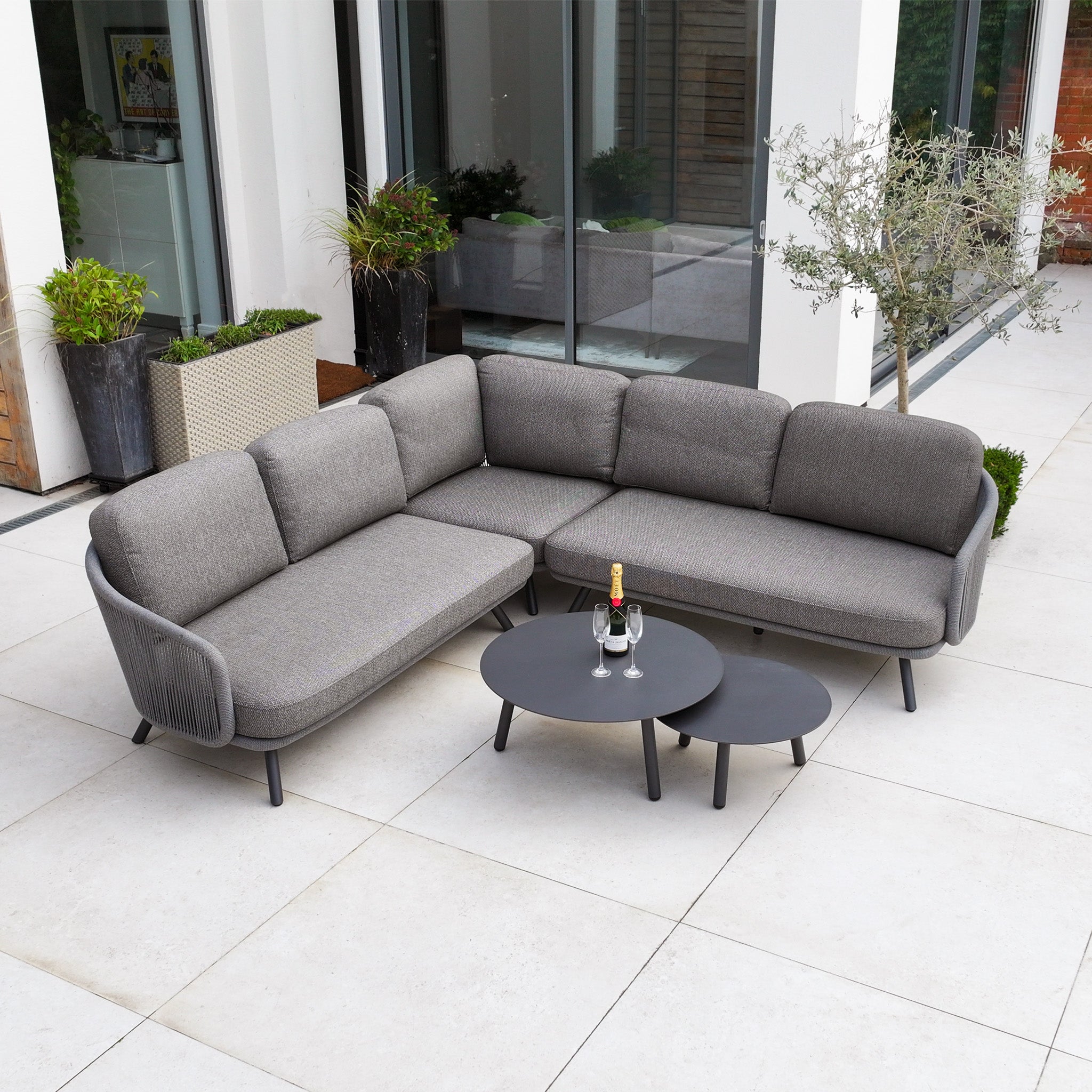 Dekota Corner Sofa Set in Charcoal with hydrophobic rope weave, paired with two round black tables, wine bottle, and glasses on a tiled patio.