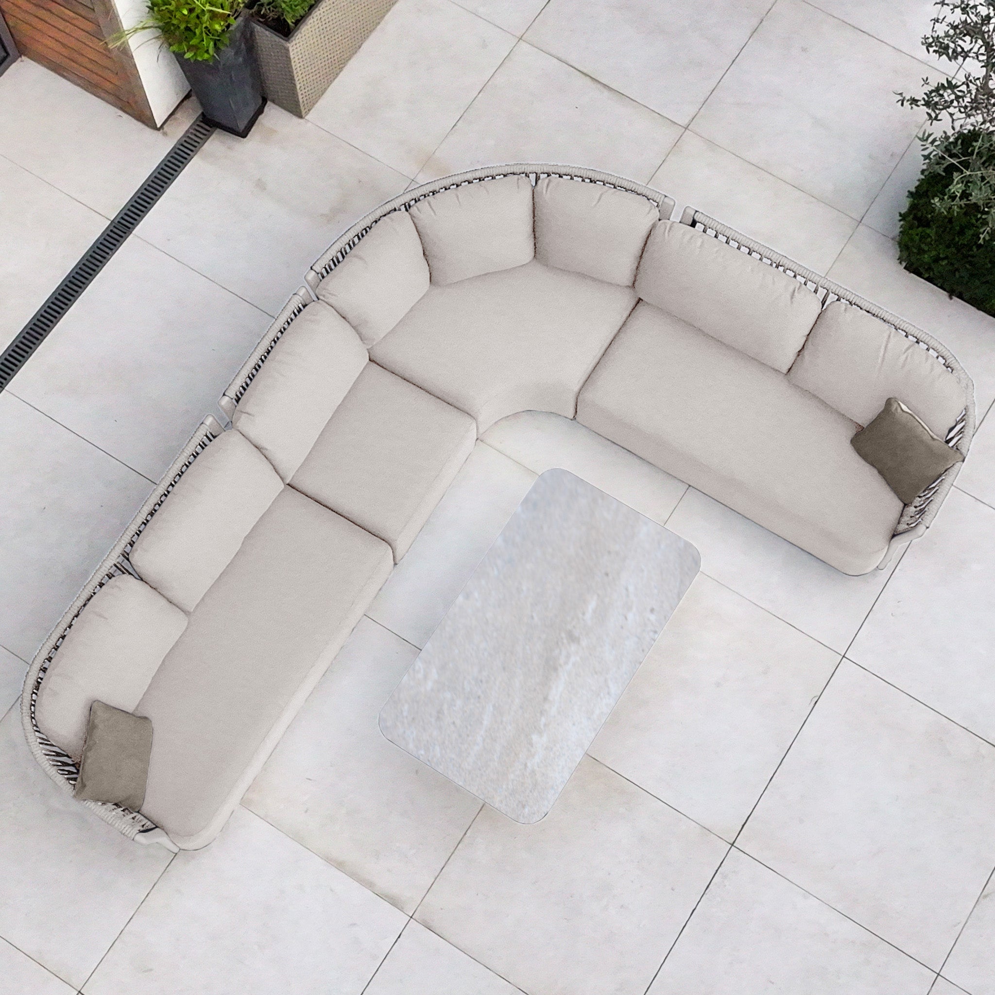 Pello Deluxe Curved Sofa Set with Altura Rising Table in Fawn, featuring quick-dry garden cushions and a rectangular table, arranged on a tiled patio and viewed from above.