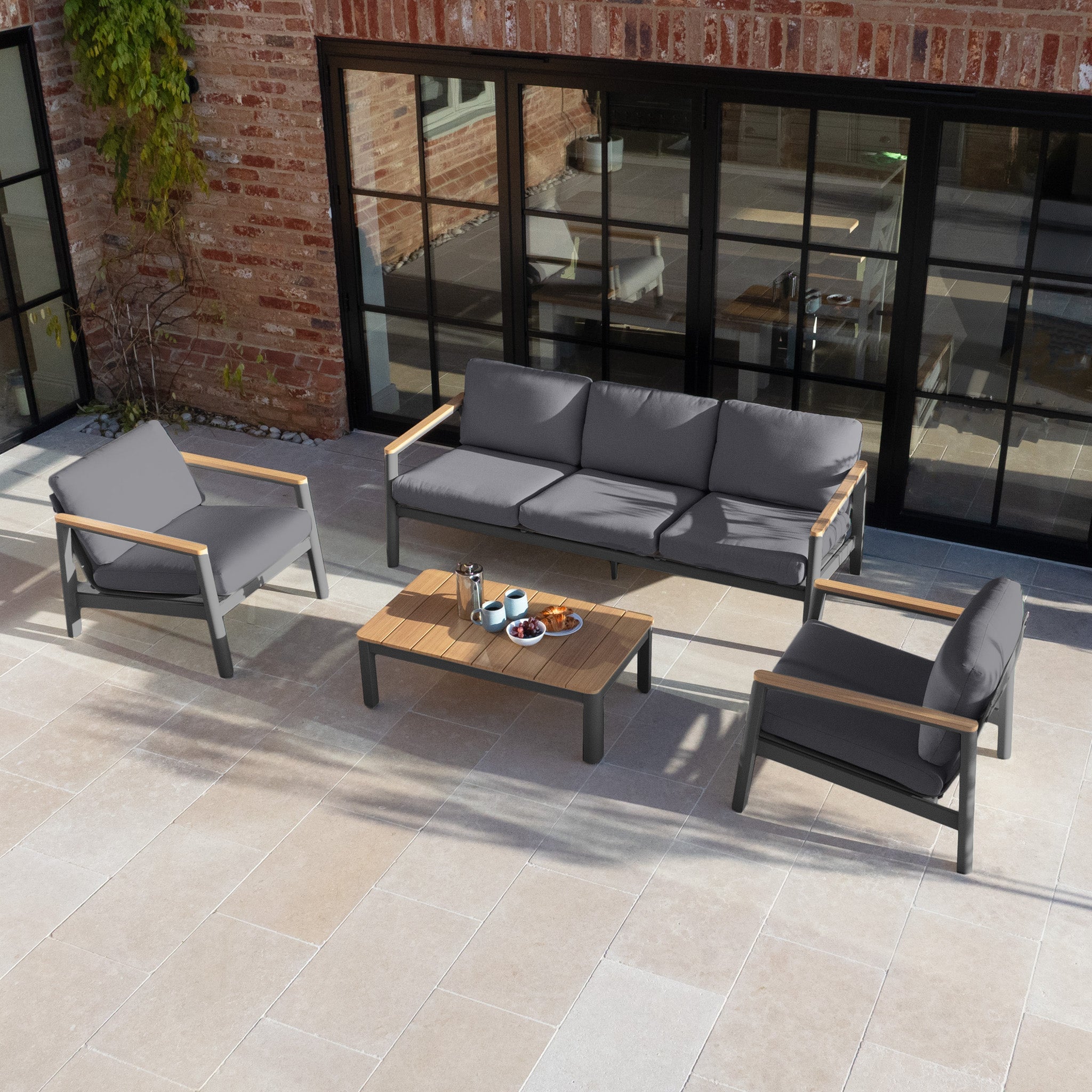 Experience modern, weather-resistant outdoor living with the Cora 3 Seat Sofa Set in Grey, plus two chairs and a coffee table, perfect for your stylish stone-tiled patio.