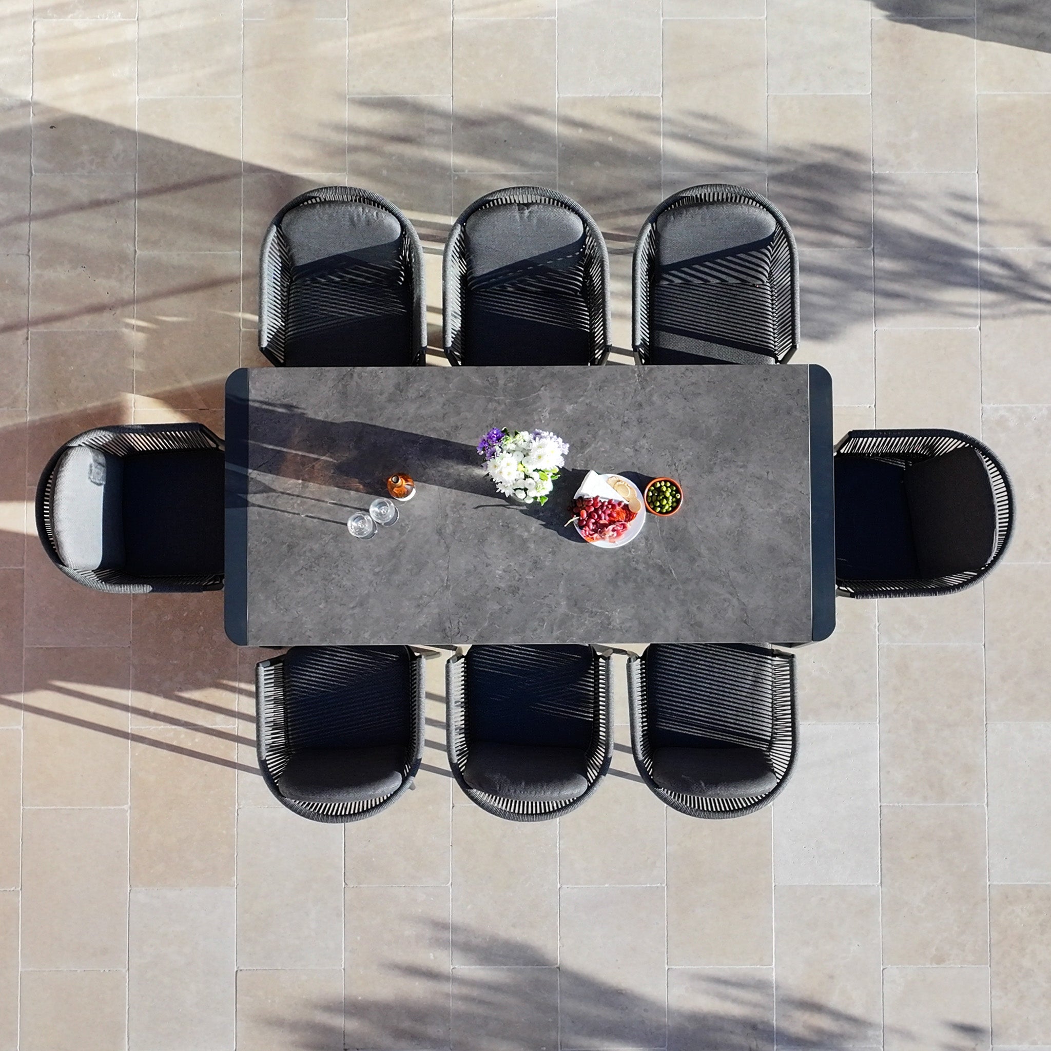The Ravona 8 Seat Rope Extending Dining Set (207-277cm) in Charcoal is beautifully arranged outdoors with flowers, snacks, and drinks, as viewed from above.