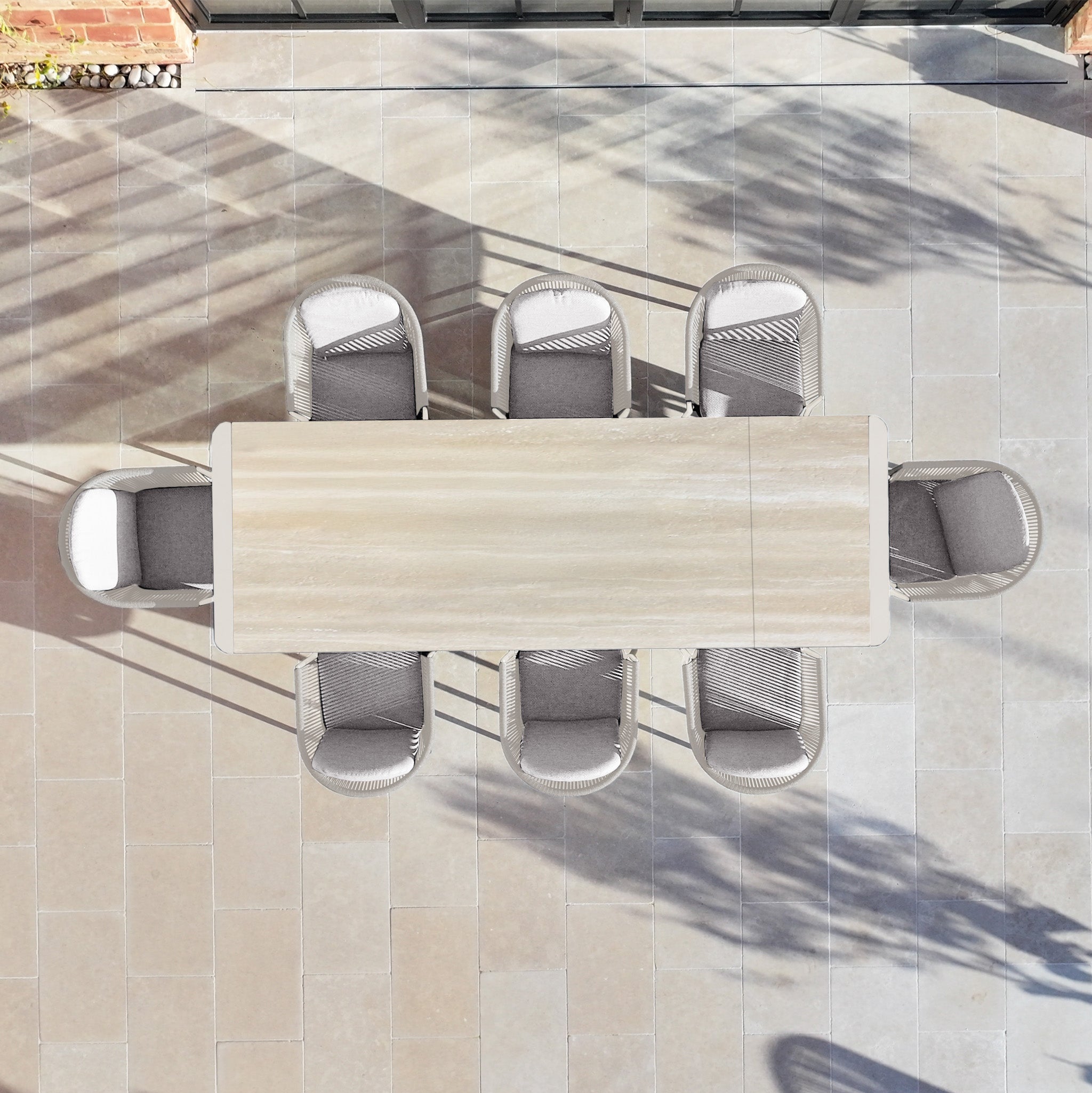The Ravona 8 Seat Rope Extending Dining Set (207-277cm) in Latte, with cushioned chairs, sits on a tiled patio—perfect garden furniture for outdoor gatherings, viewed from above.