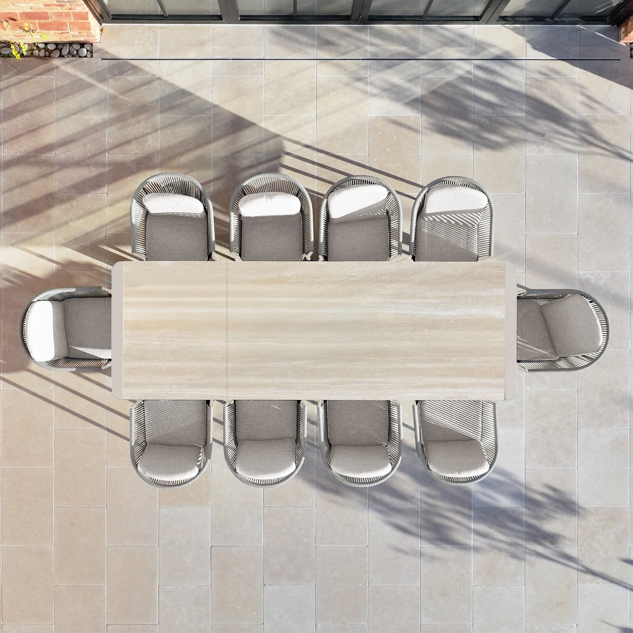 A Ravona 10 Seat Rope Extending Dining Set (207-277cm) in Latte, featuring a rectangular table and matching chairs, is displayed elegantly on a tiled patio and viewed from above.