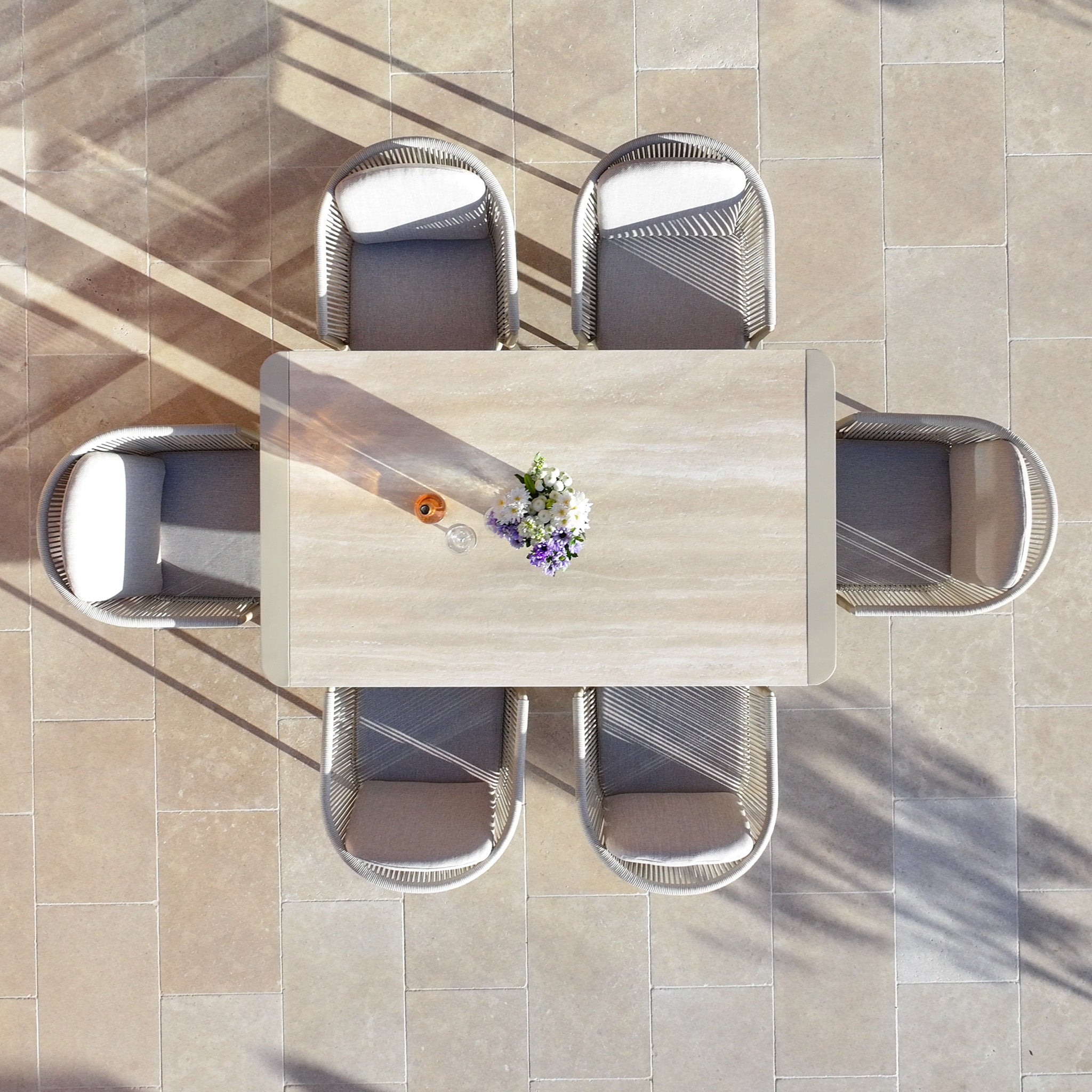 Overhead view of the Ravona 6 Seat Rope Extending Dining Set (162-222cm) in Latte, with flowers and drinks, surrounded by four chairs on a tiled patio; sleek aluminium frame adds modern appeal.