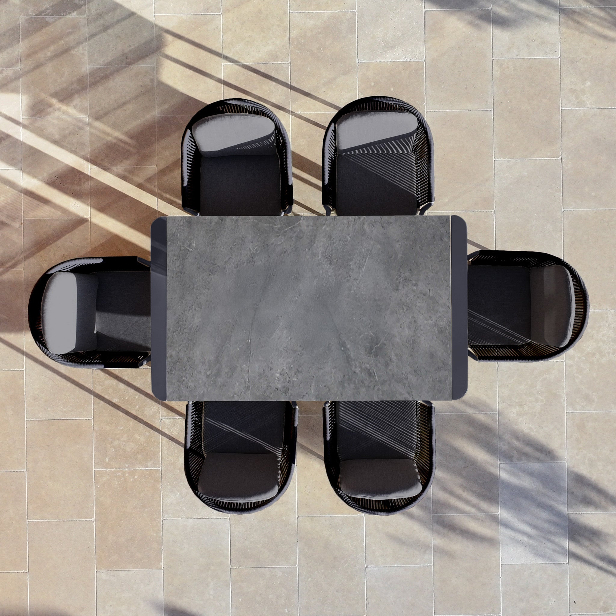 Top view of the Ravona 6 Seat Rope Extending Dining Set (162-222cm) in Charcoal with six black chairs on a tiled patio, casting long shadows.