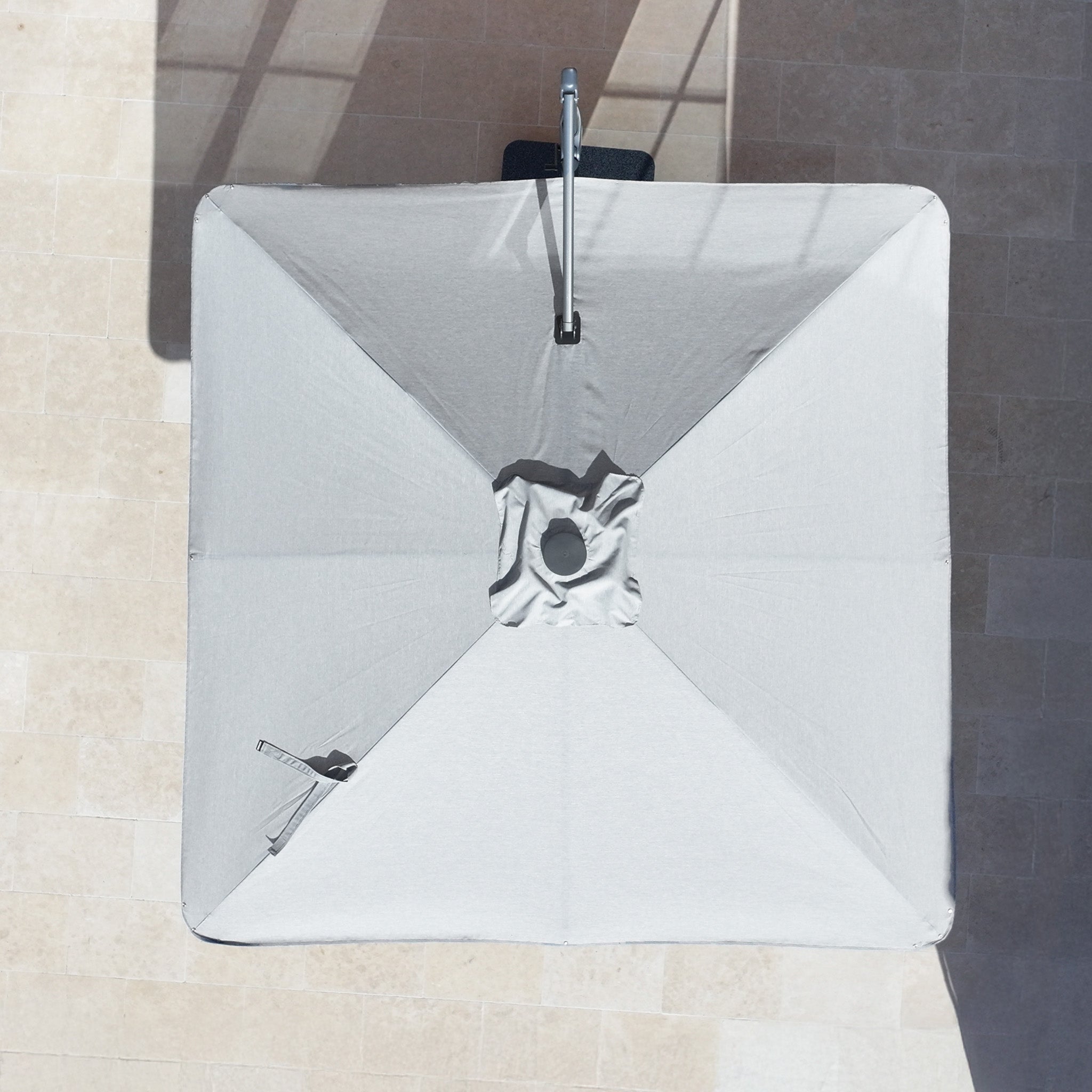 Aerial view of the Nexus T2 Premium 3m Square Cantilever Parasol in Manhattan Grey with 90kg granite base, casting a shadow on light tiles and highlighting its elegant design and practical 360° rotation.