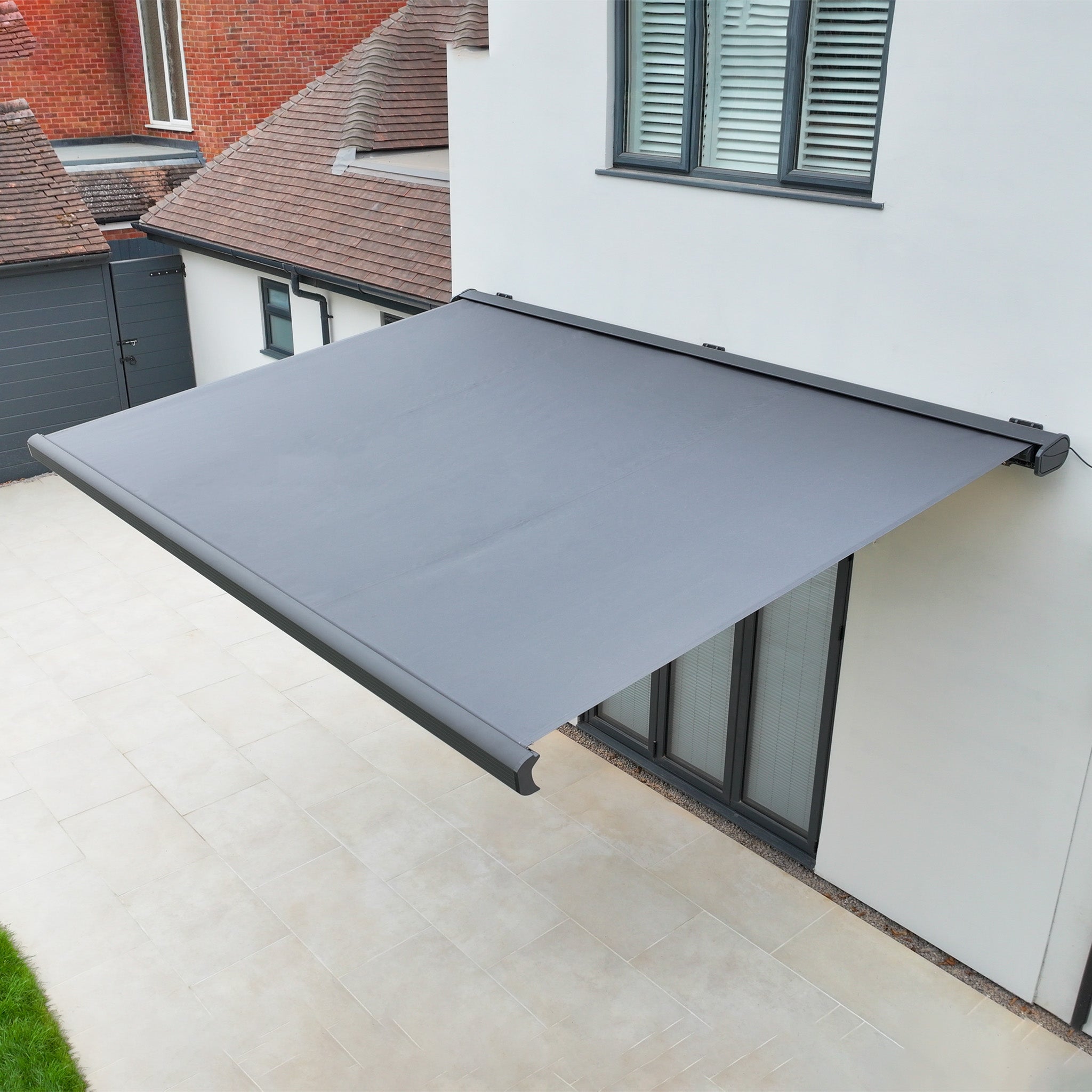 The 3m x 2m Electric Motorised Awning in Grey, featuring waterproof acrylic fabric, extends over a patio beside a modern light-walled house.