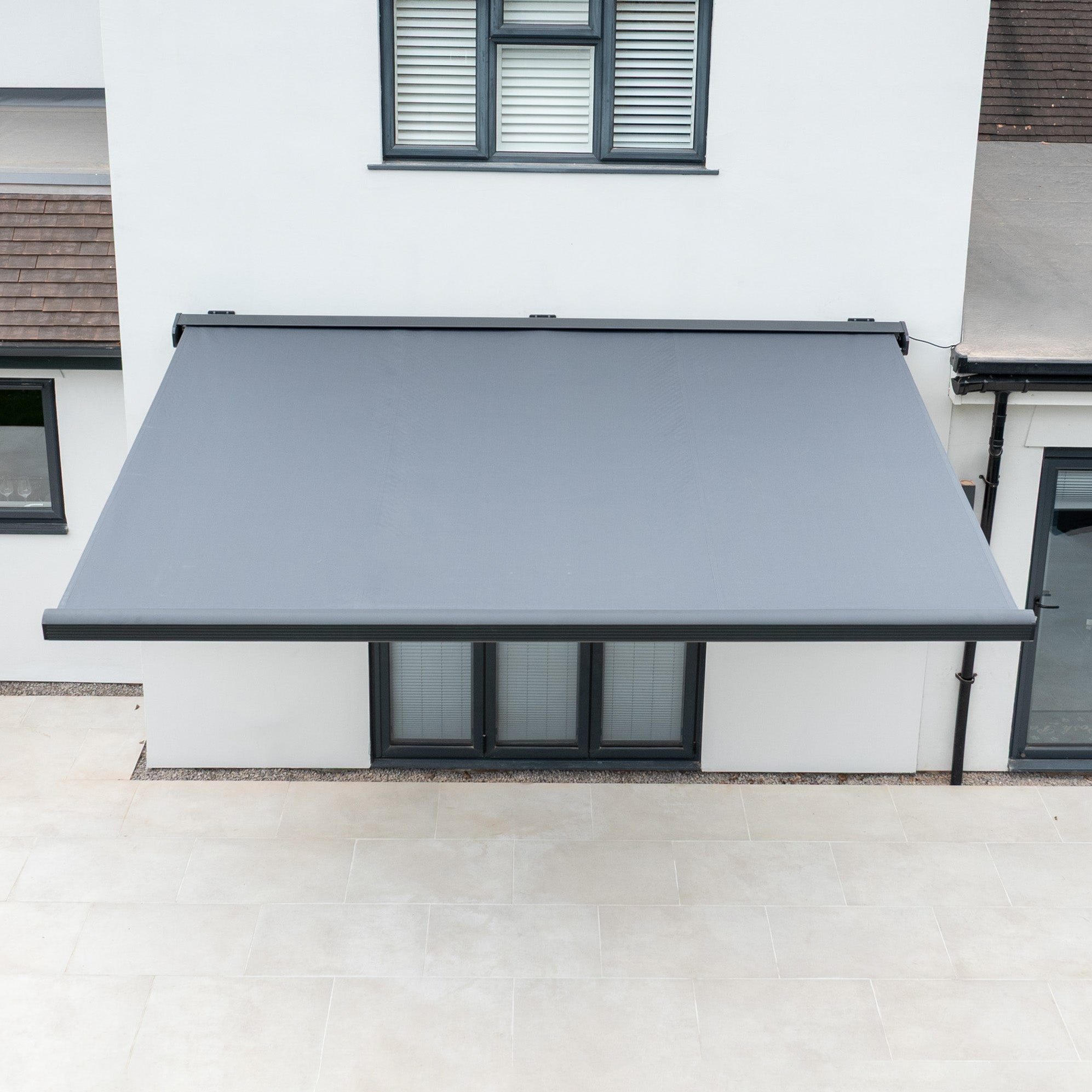 A 3m x 2m Electric Motorised Awning in Grey with waterproof acrylic fabric is installed over patio doors on a modern white house.