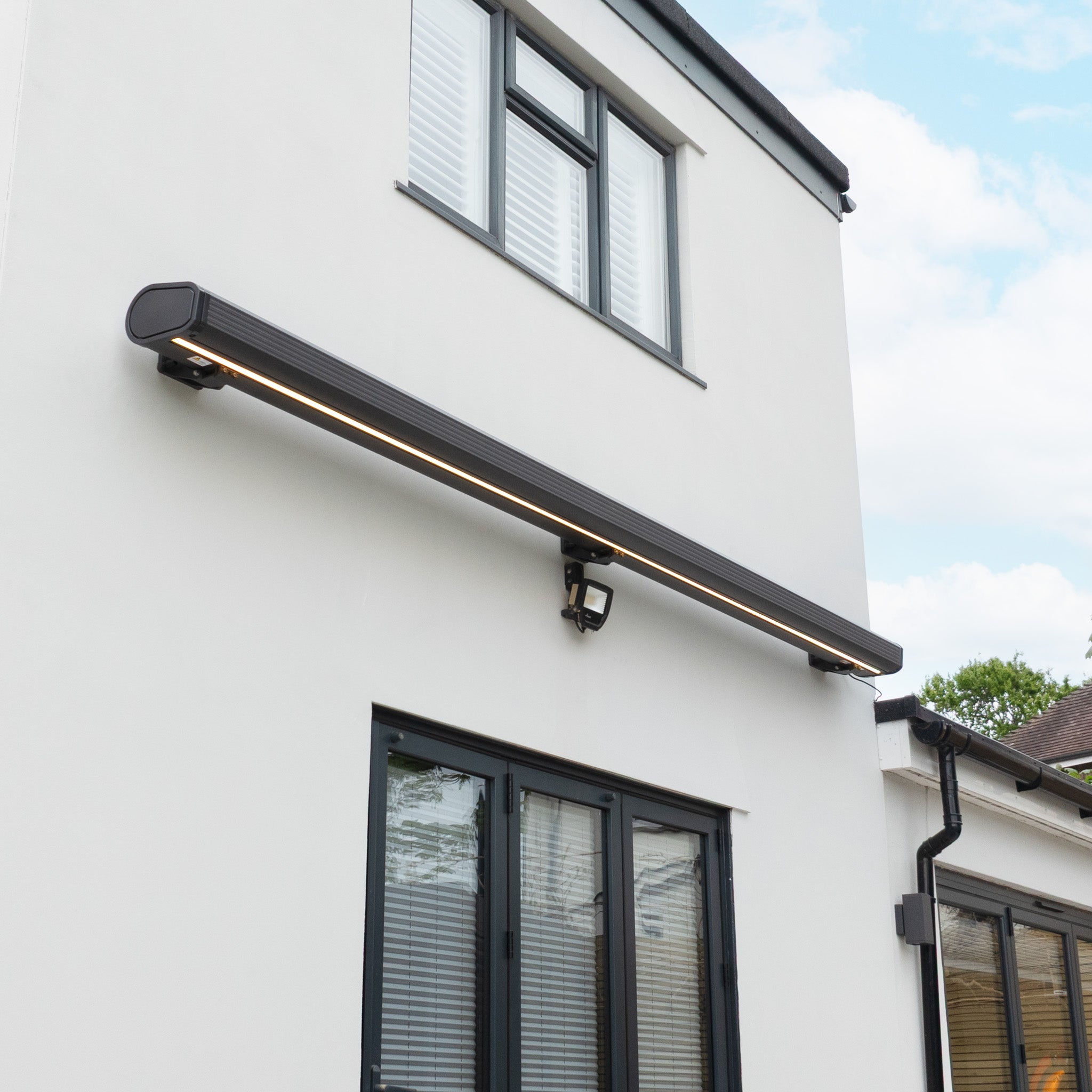 A 3m x 2m Electric Motorised Awning in Grey with waterproof acrylic fabric extends above double glass doors on a modern white house exterior.