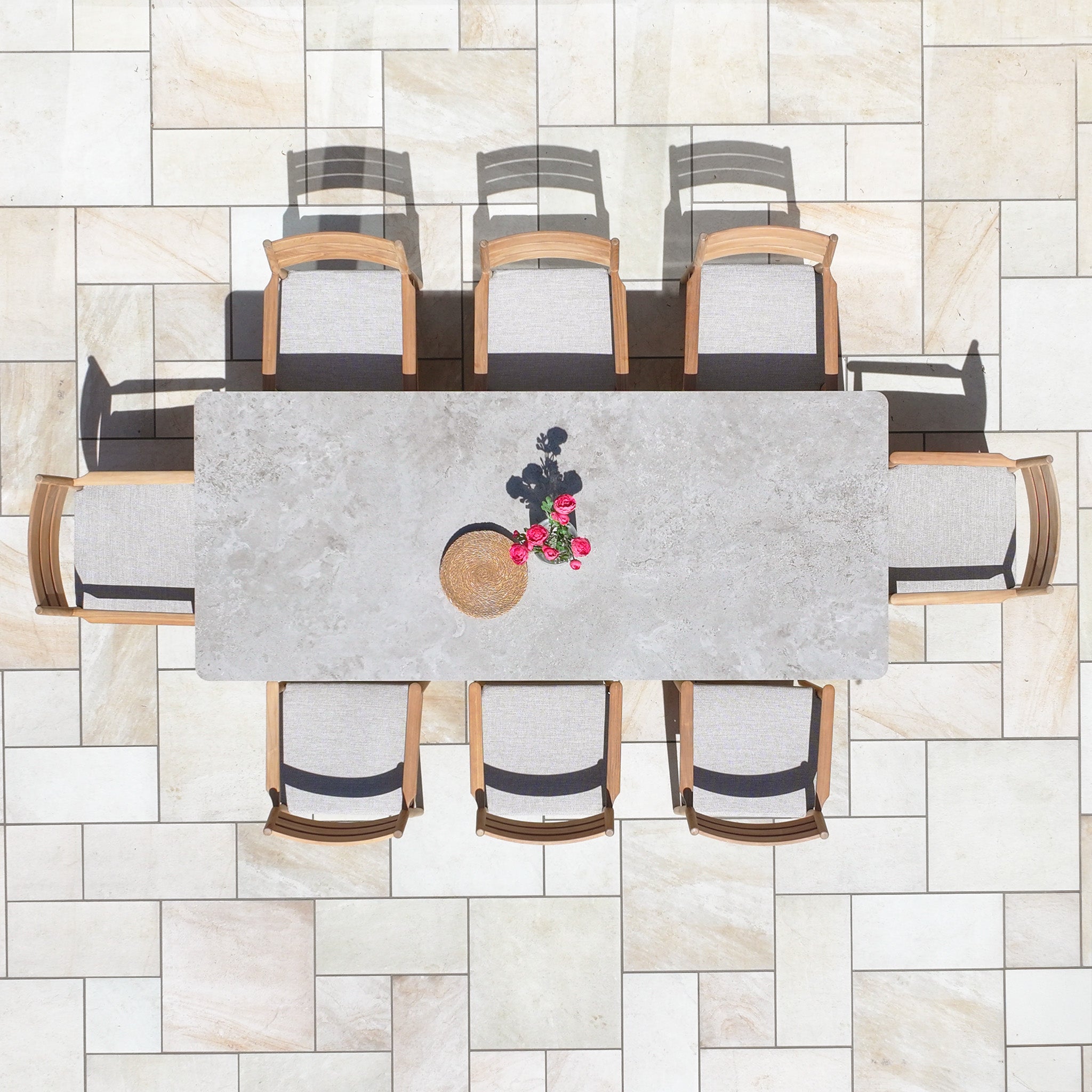 The Siena 8 Seat Dining Set with Ceramic Top Table in Fawn, shown from above, includes eight chairs and is styled with a small plant and a bowl on a tiled patio.