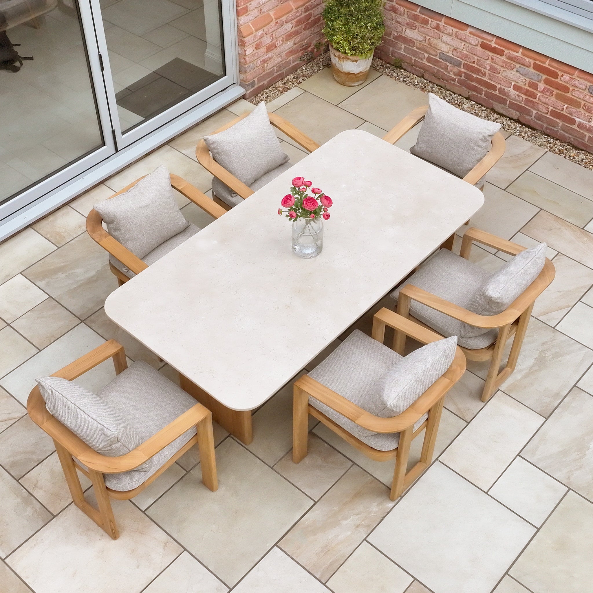 The Tivoli 6 Seat Dining Set with Marble Dining Table in Fawn, complete with six cushioned chairs, is elegantly arranged on the tiled patio floor.