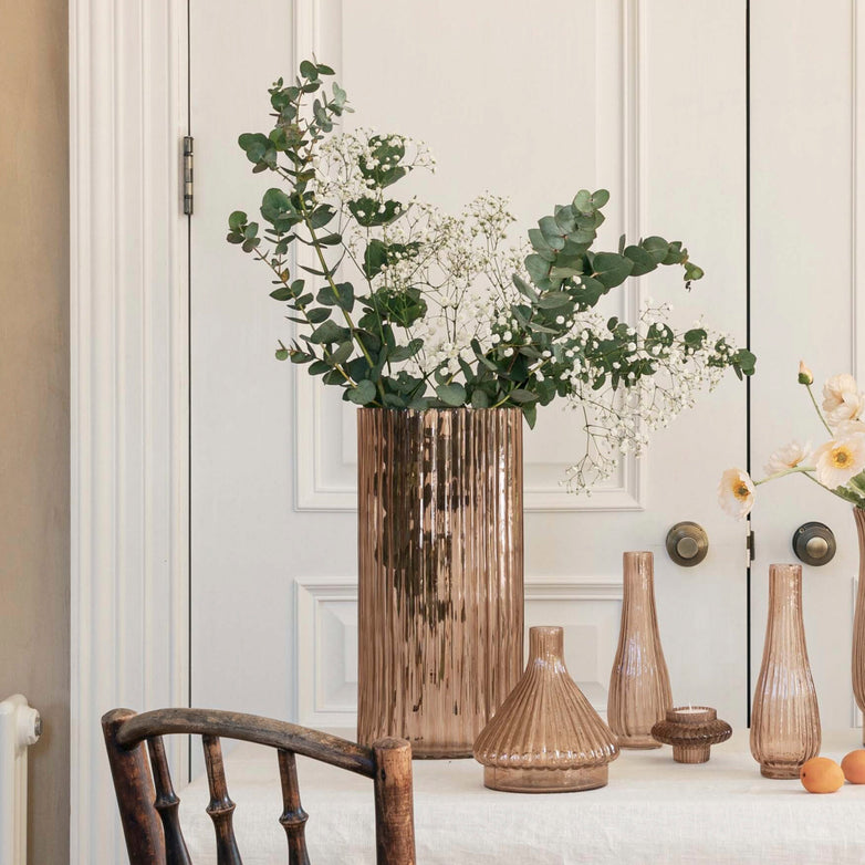 The table features the Ivyline Daphne Large Ribbed Vase in Apricot, elegantly filled with greenery and paired with smaller brown vases, enhancing the sustainable décor against a classic white paneled door backdrop.