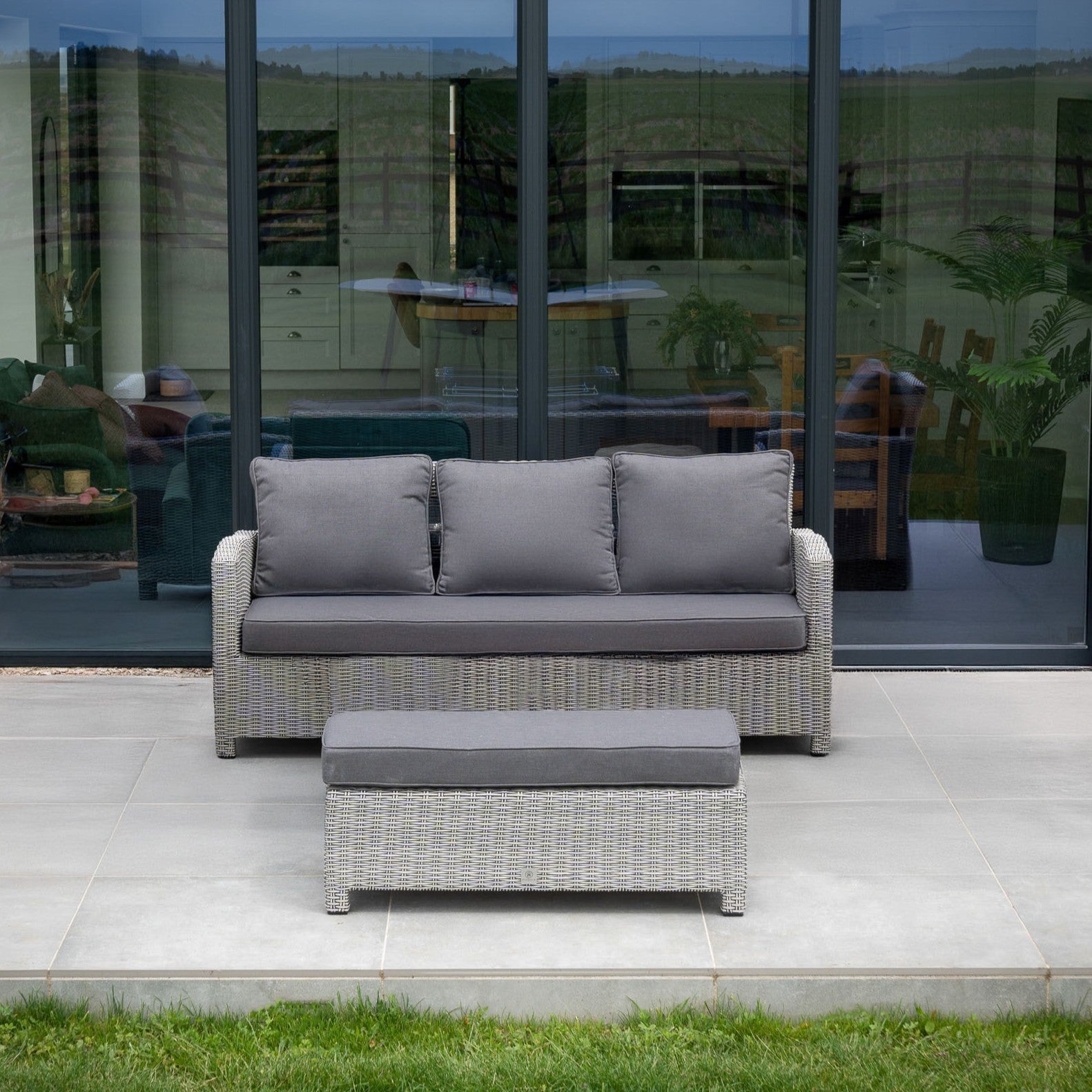 A Santiago 3 Seat Sofa and Bench in white wash sit on a patio in front of large glass doors with reflections.