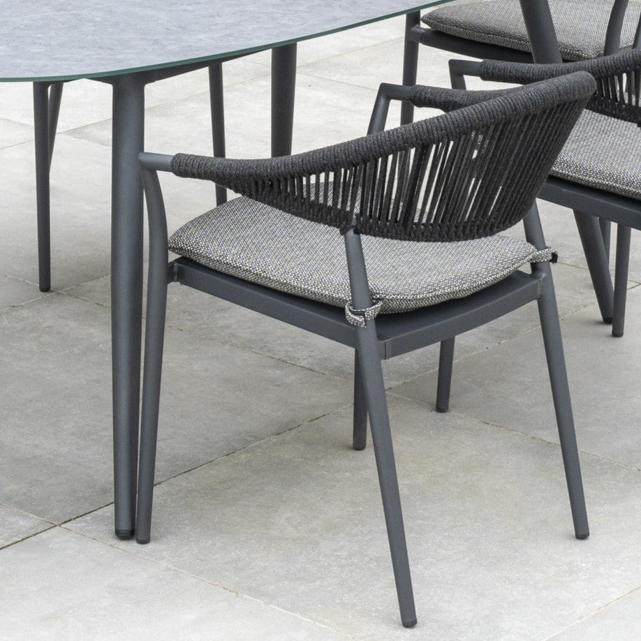 Cloverly 6 Seat Rope Oval Dining Set with Ceramic Table in Charcoal on the patio, featuring a black outdoor chair with a rope backrest and gray cushion.