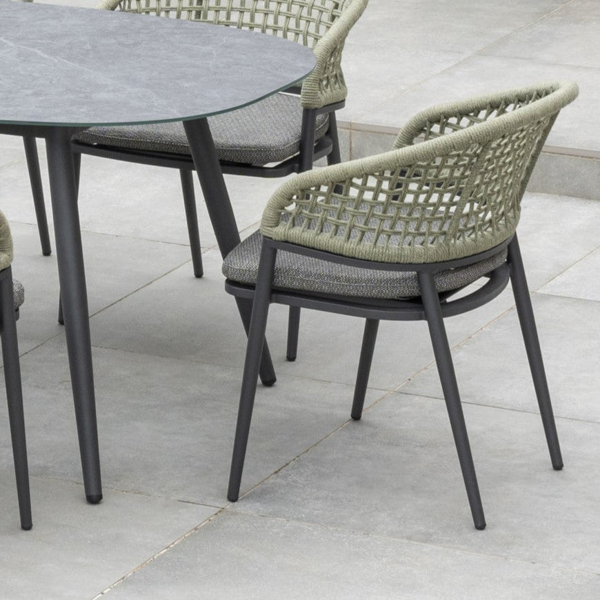 The Kalama 8 Seat Rope Oval Dining Set with Ceramic Table in Olive Green features woven chairs around a gray table, ideal for a stone patio. Crafted from weatherproof aluminum, it offers lasting durability and style for alfresco dining.