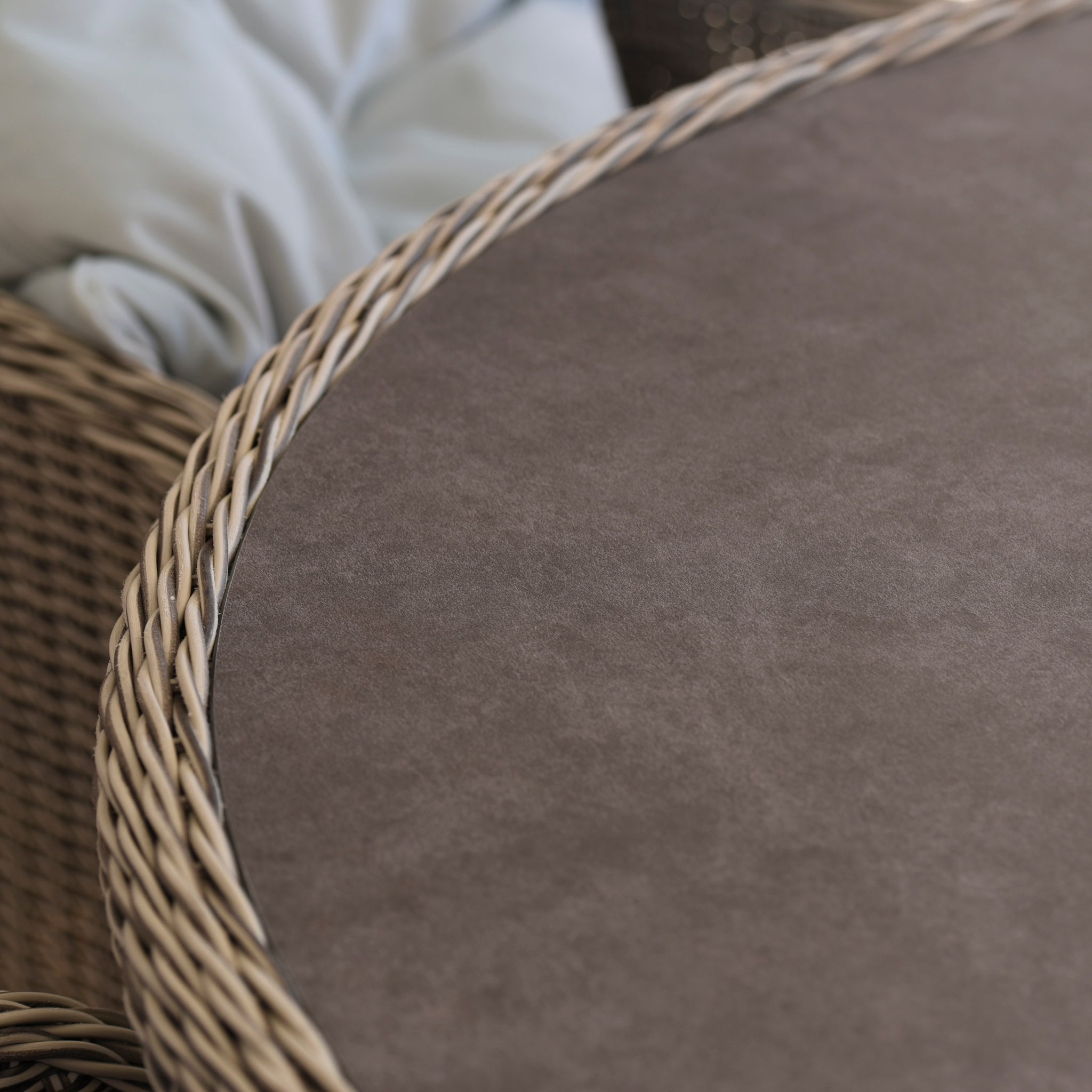 Close-up of the Santiago 180cm x 120cm Firepit Oval Dining Table in White Wash with a smooth surface and part of a woven chair, perfect for stylish outdoor furniture settings.