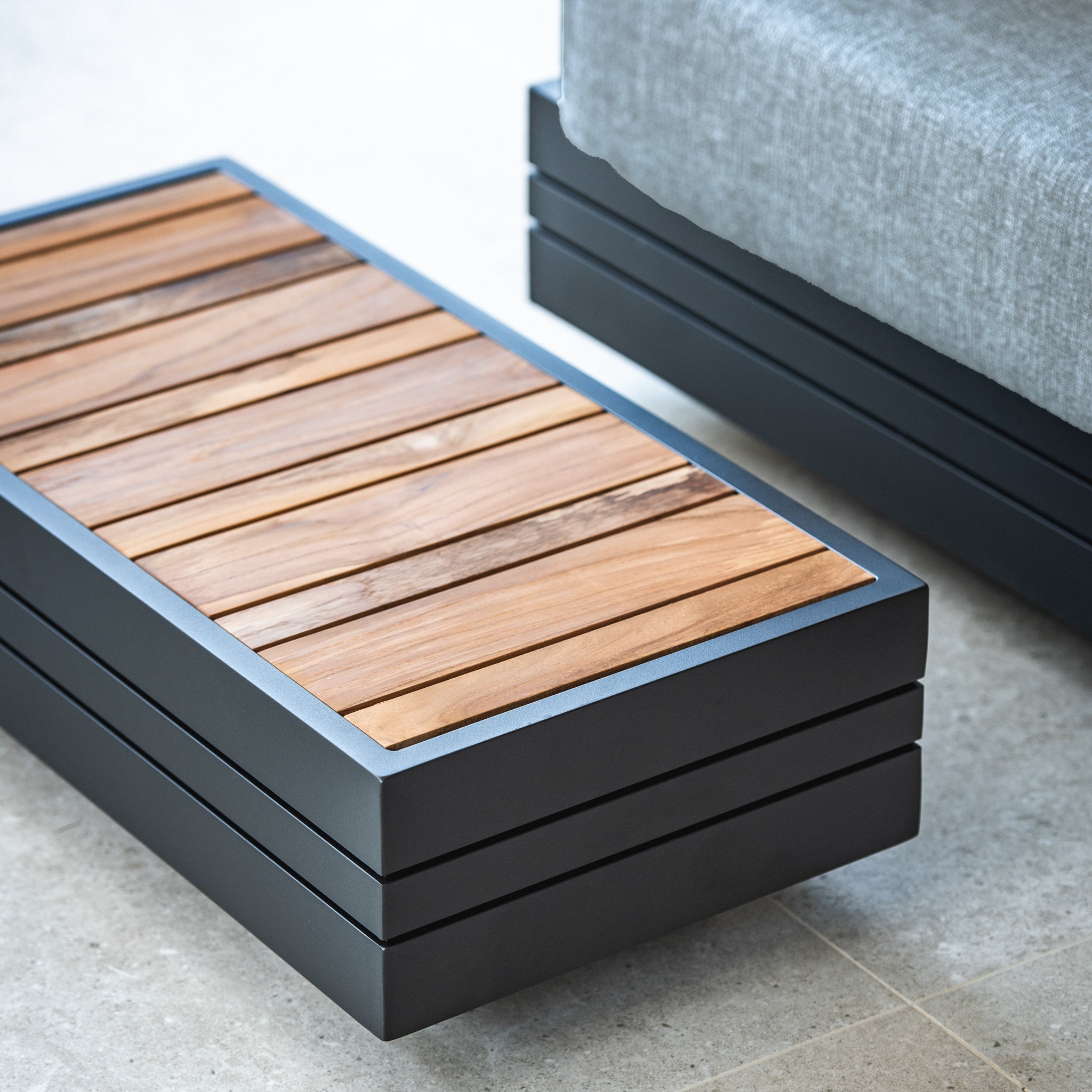 Modern wooden and metal outdoor coffee table next to a gray cushioned chair, part of our Panama Luxury Outdoor L-Shape Corner Group Set in Washed Grey featuring sustainable teak.