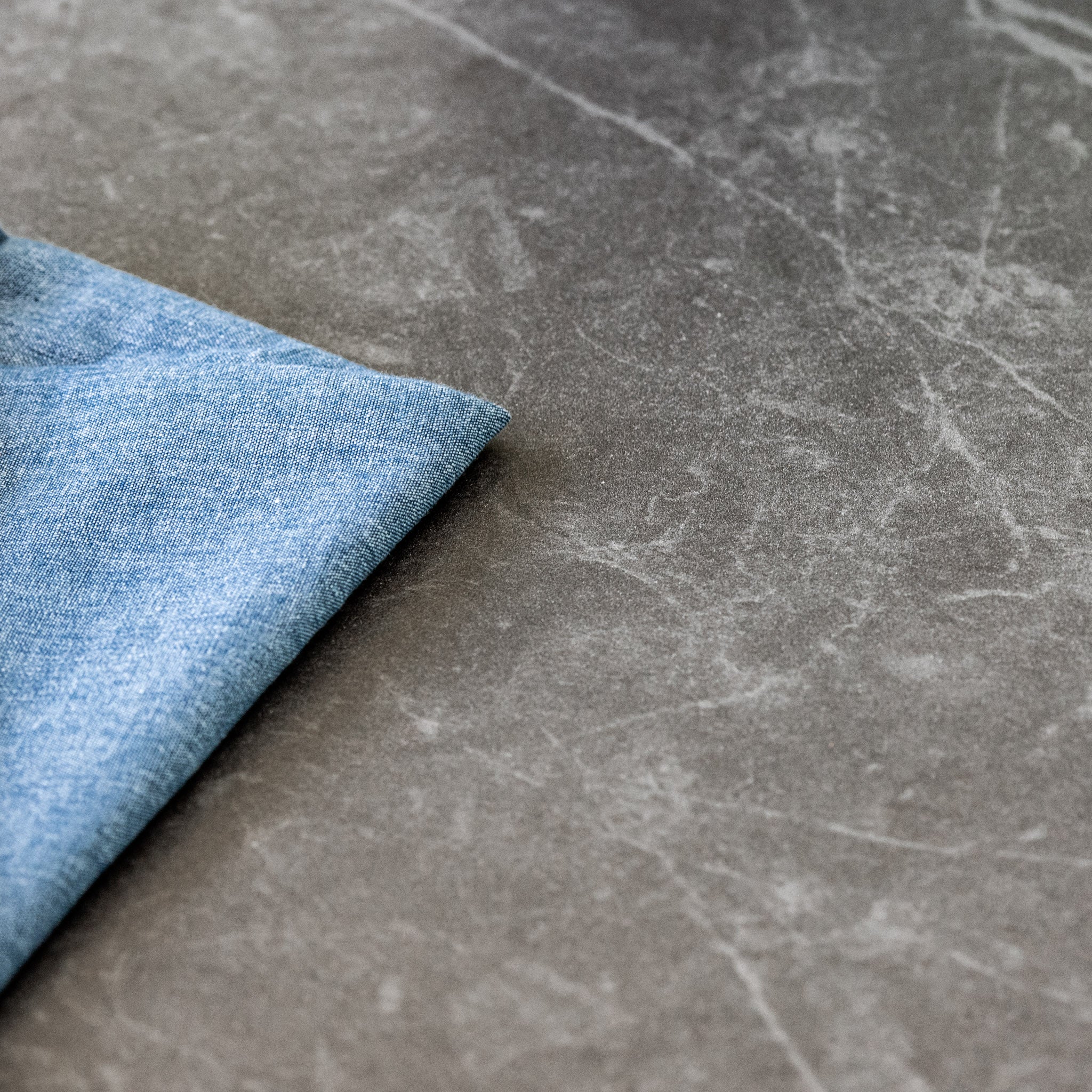 Close-up of a folded blue denim fabric on a grey marble surface, perfectly complementing the sophisticated aesthetic of the Cloverly 6 Seat Rope Oval Dining Set with Ceramic Table in Charcoal.
