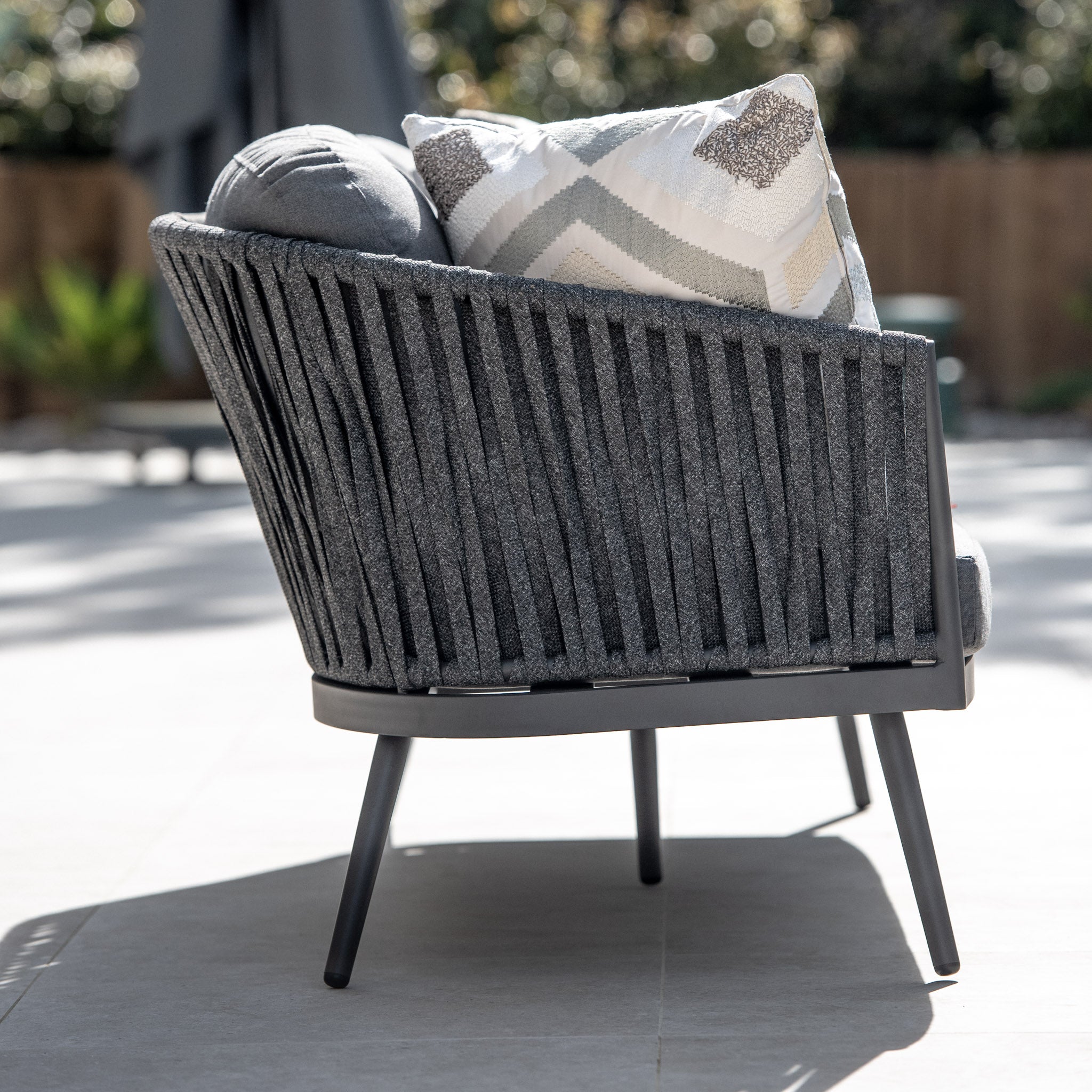 Grey outdoor chair with cushions, featuring a slatted backrest, perfectly complements the Harbour Lifestyle Monterrey 3 Seat Rope Sofa Set with Rising Firepit Table in Grey on the patio.