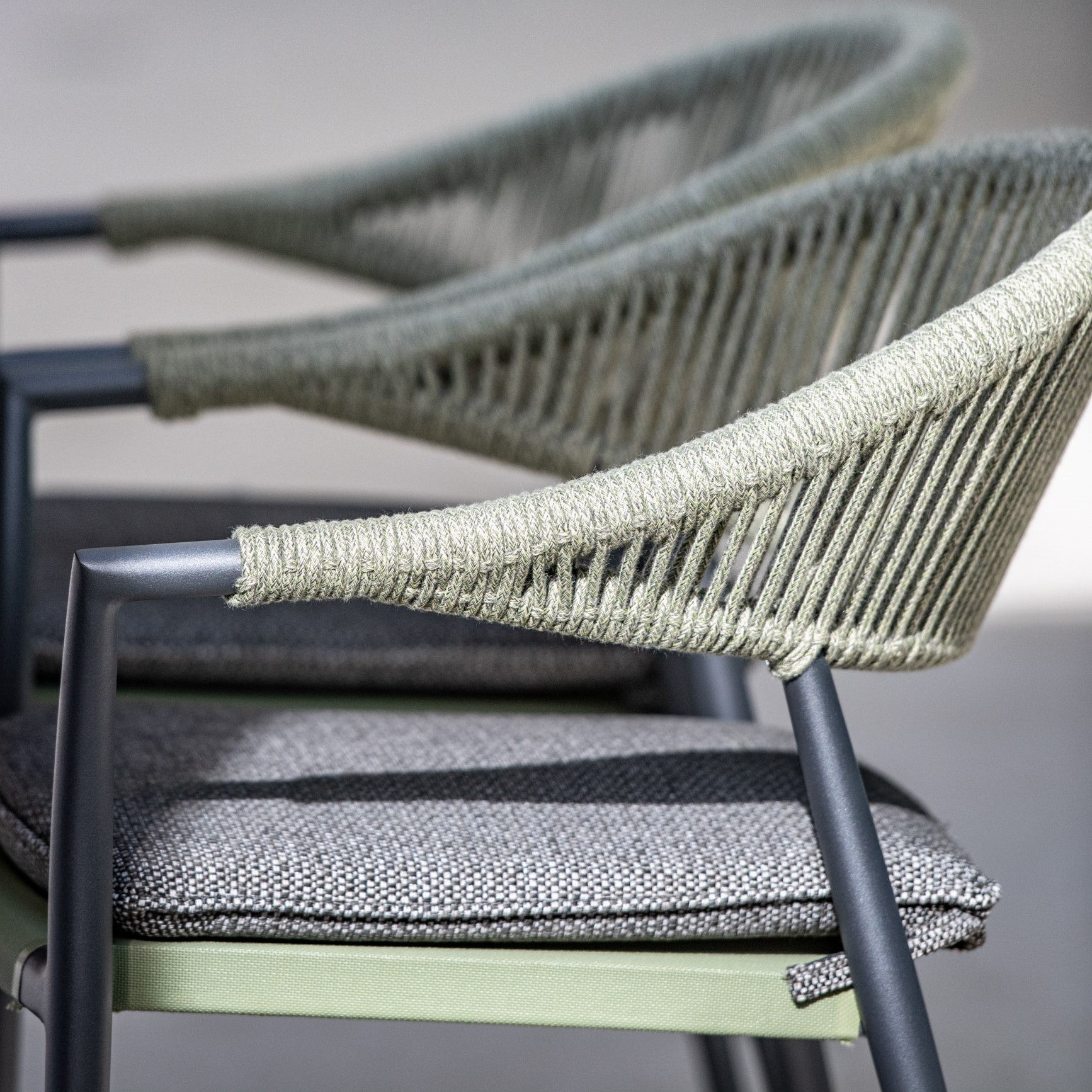 Close-up of three modern Cloverly 8 Seat Rope dining chairs with olive green armrests and grey cushioned seats, perfectly aligned in a row.