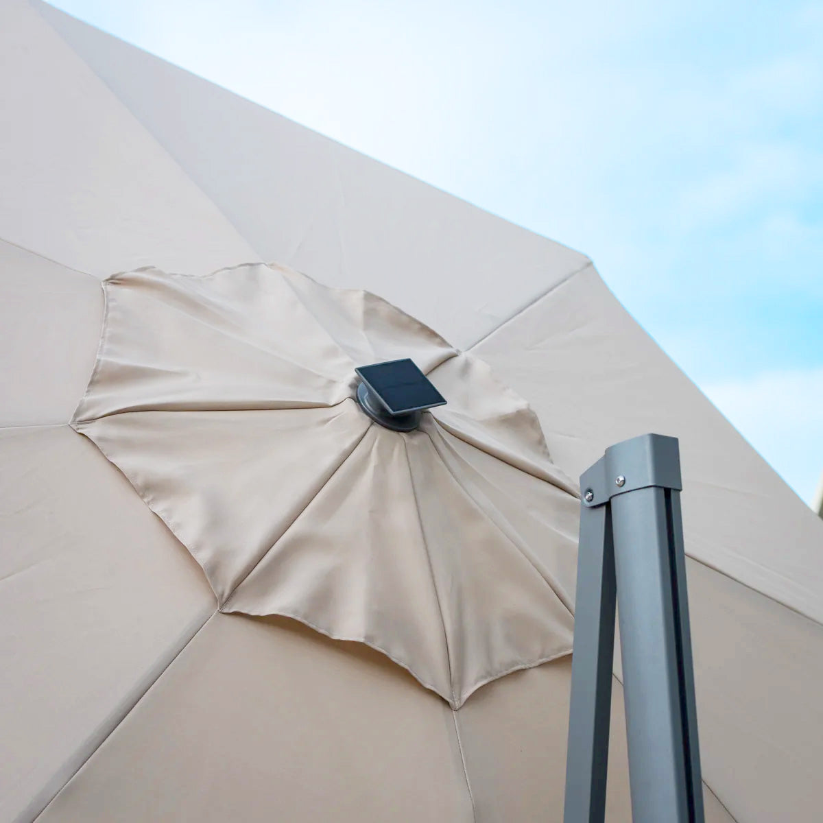 The Ares 3.5m Round Cantilever Parasol in Beige, featuring solar-powered LED lights, is elegantly displayed against a blue sky.