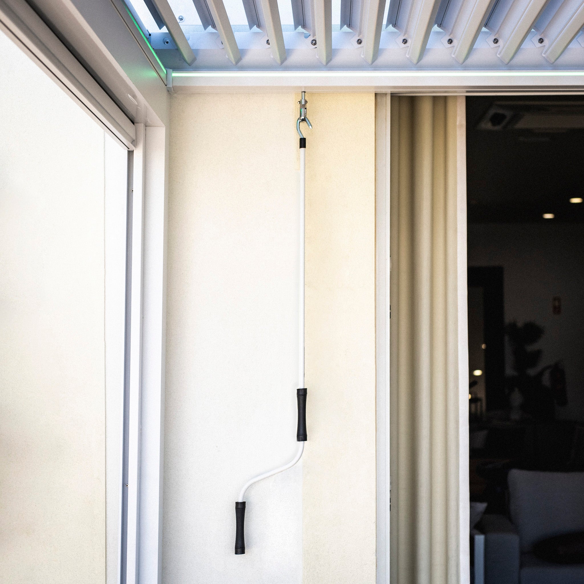 The PergoSTET Plus 4m x 4m Square Pergola, featuring a sleek white frame, complements your modern décor with its contemporary design and black accents. Its elegant finish enhances the view through the sliding glass door and perfectly suits any setting near a window.
