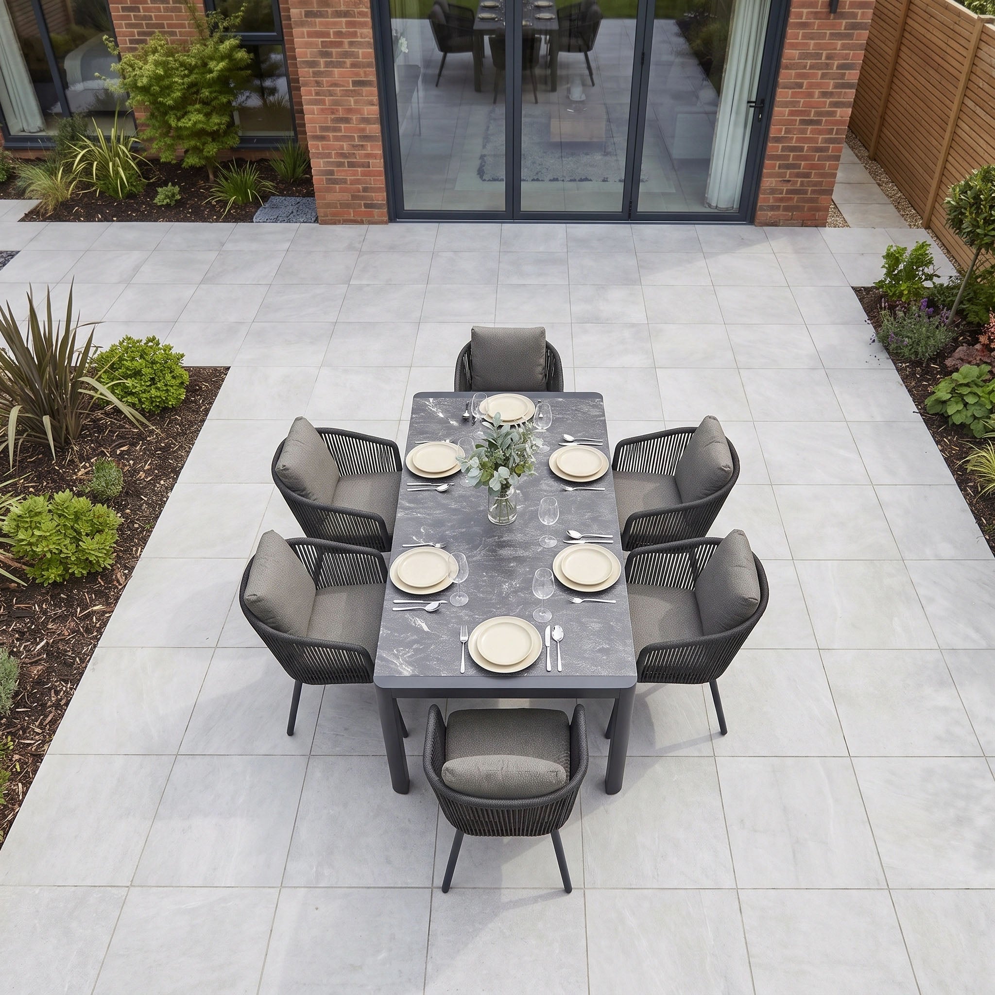Dekota 6 Seat Dining Set with Ravona Extending Table in Charcoal, arranged on a tiled patio and set with plates, cutlery, and a small centerpiece.