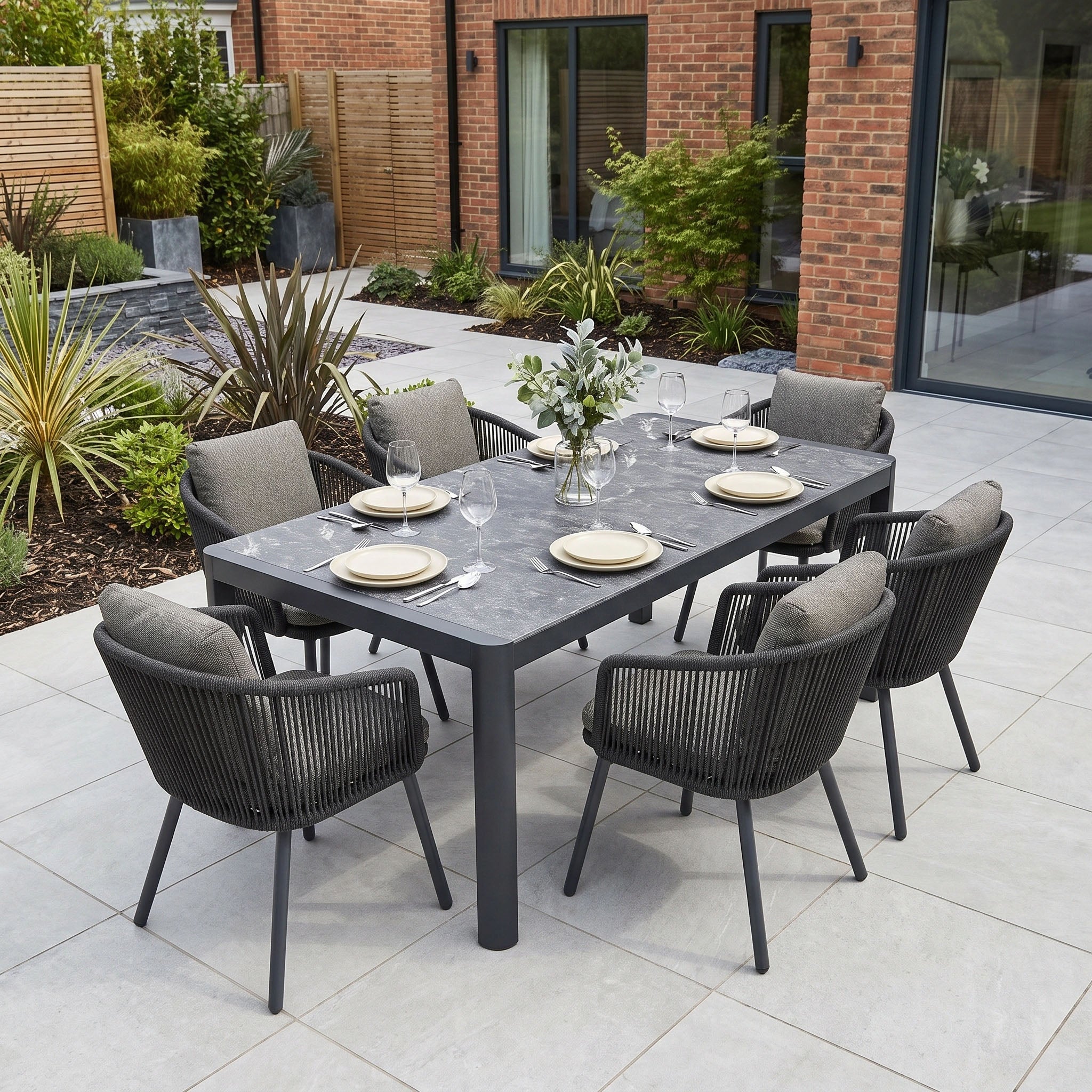 Experience stylish outdoor dining with the Dekota 6 Seat Dining Set, featuring plush-cushioned gray Dekota Dining Chairs and a versatile Ravona Extending Table in Charcoal. Beautifully surrounded by modern patio greenery, this elegant aluminium set combines comfort and sophistication to create the perfect setting for memorable gatherings.