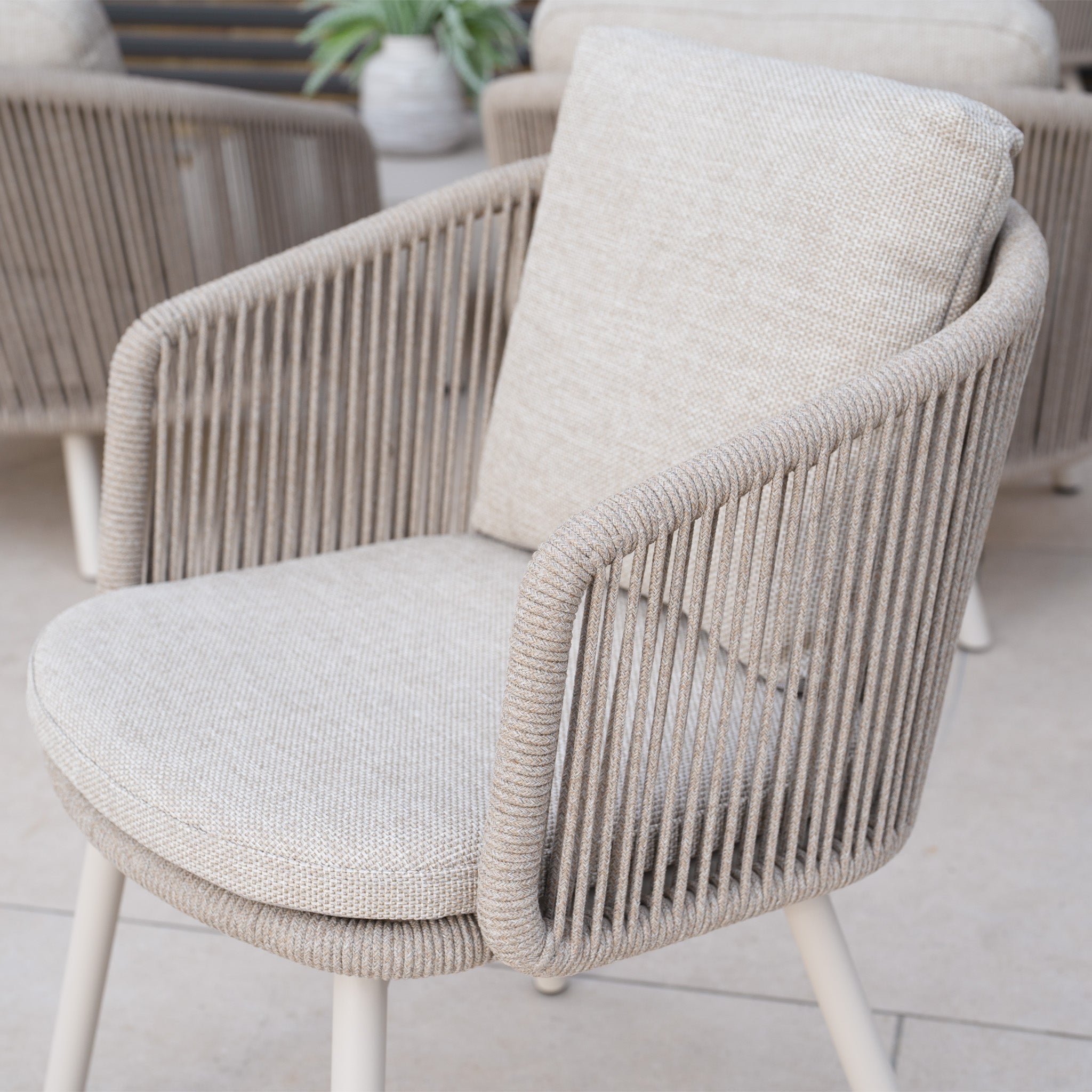 A Dekota Dining Chair in Fawn, featuring beige cushions with woven rope arms and backrest, is set on a tiled floor.