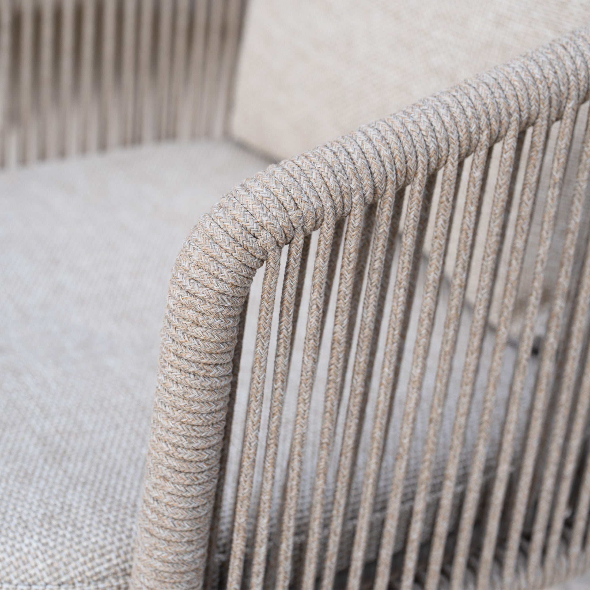 Close-up of the Dekota Dining Chair in Fawn, featuring a woven rope armrest and a beige textured cushion.