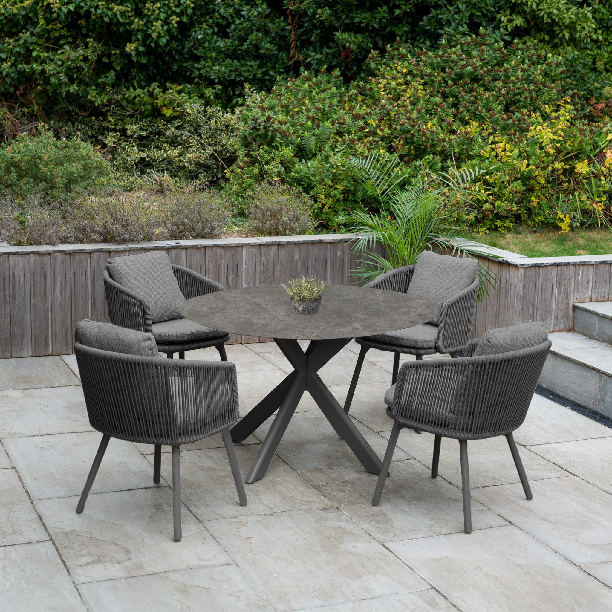 The Dekota 4 Seat Round Rope Dining Set with Albatross Table in Charcoal features four cushioned chairs, offering a stylish and comfortable outdoor dining experience.