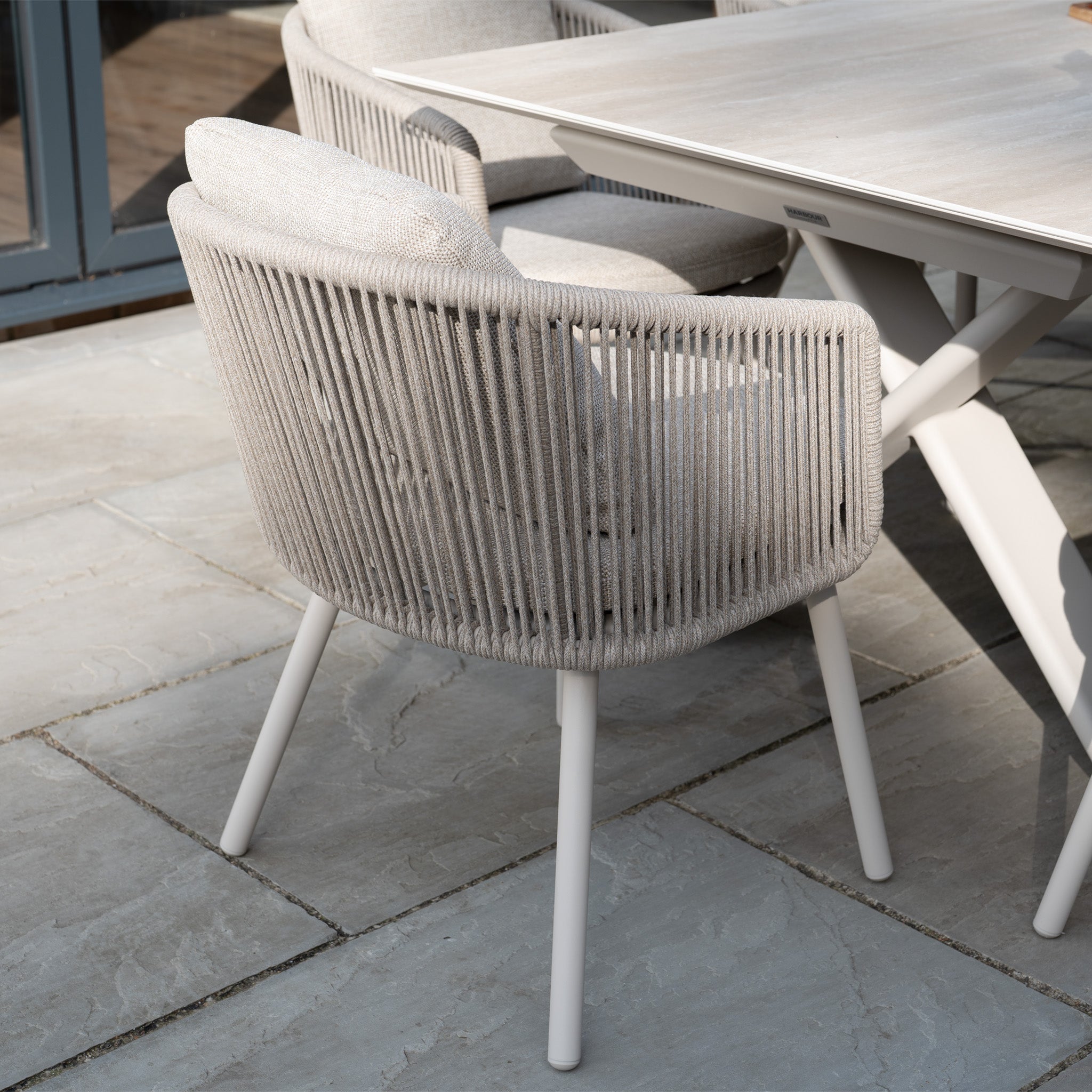 The Dekota 6 Seat Rope Dining Set with Albatross Extending Table in Fawn creates a stylish outdoor dining area on the stone patio.