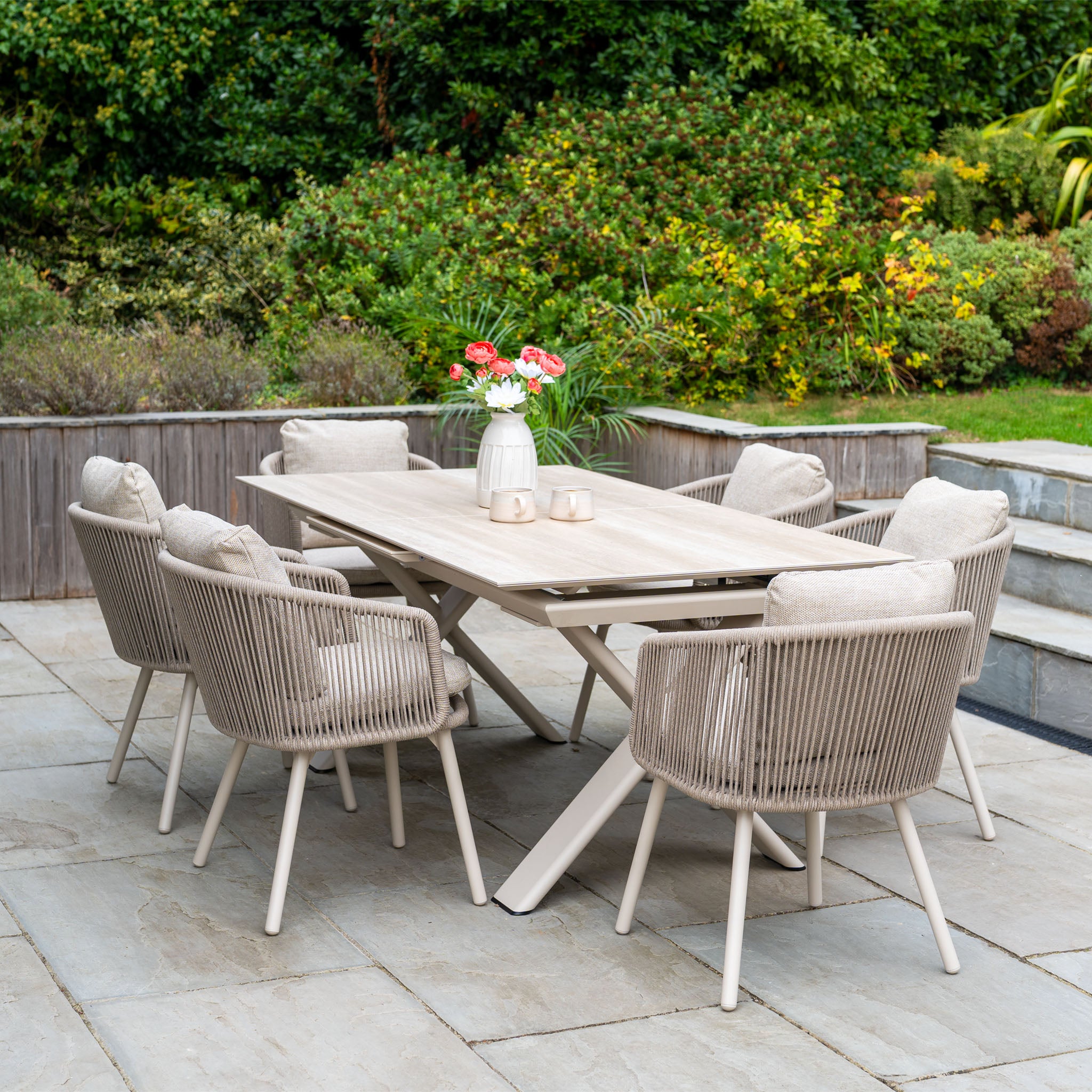 Enjoy outdoor dining with the Dekota 6 Seat Rope Dining Set featuring the Albatross Extending Table in Fawn, perfect for your patio surrounded by greenery.