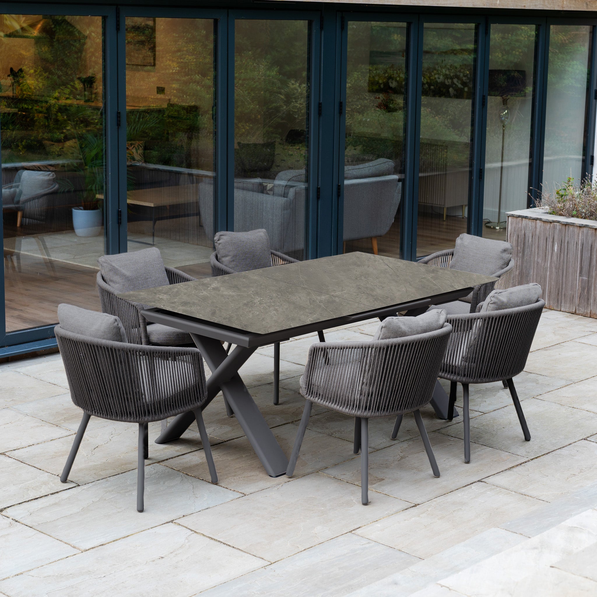 The Dekota 6 Seat Rope Dining Set with Albatross Extending Table in Charcoal features cushioned chairs and a stylish rectangular table, ideal for outdoor dining on your stone patio.