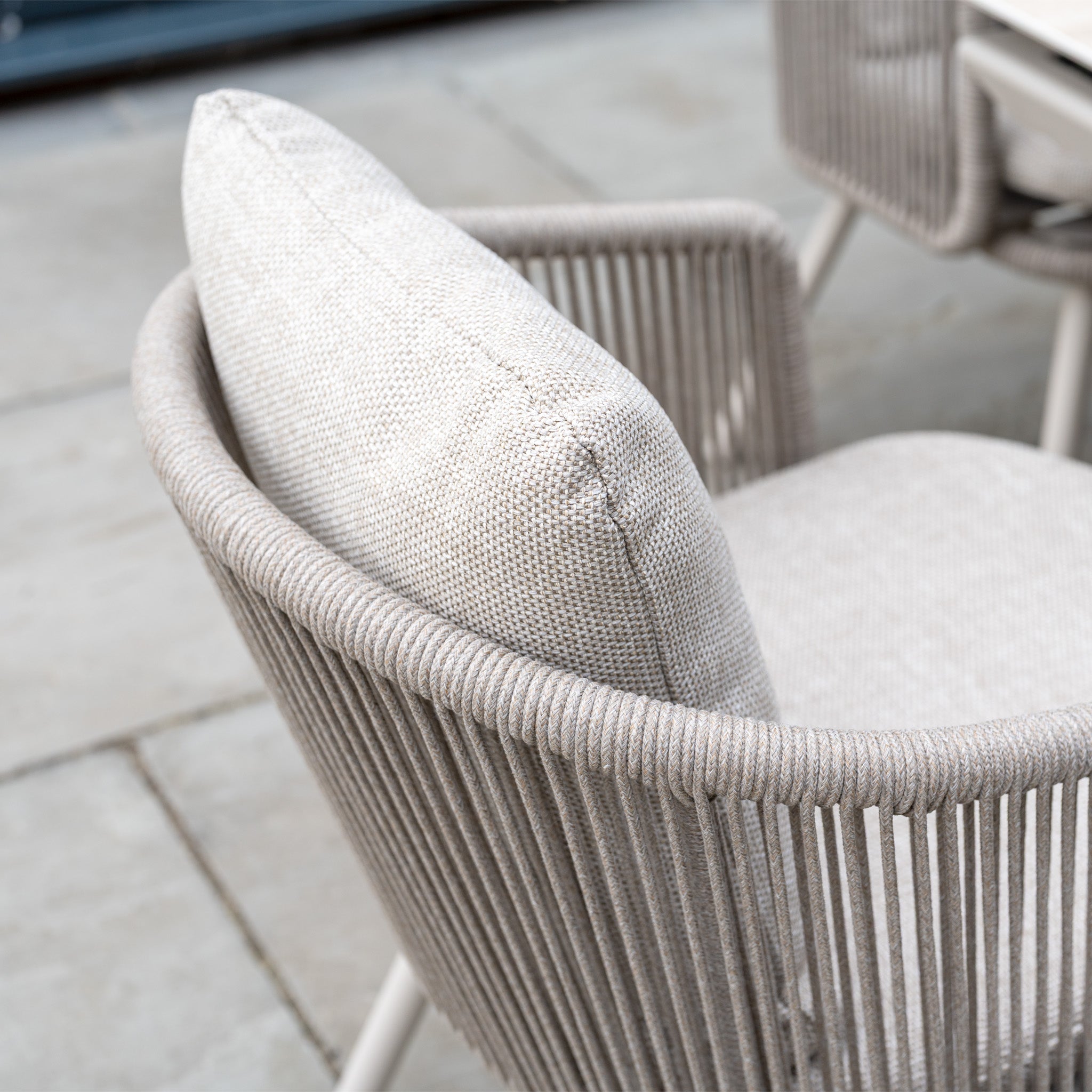 Close-up of a modern outdoor chair from the Dekota 6 Seat Rope Dining Set with Albatross Extending Table in Fawn, featuring a light beige cushion and woven rope backrest.