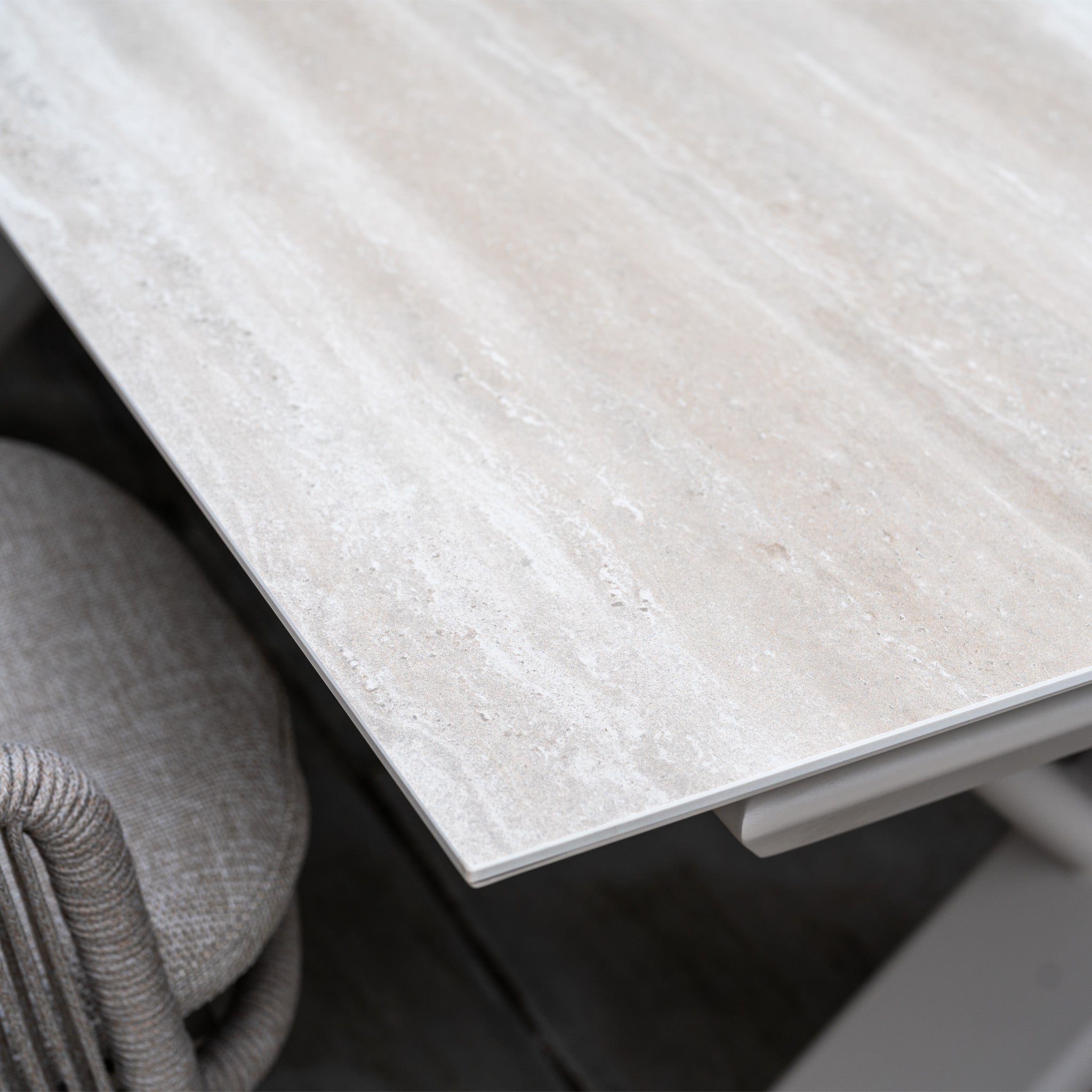 Close-up of the light fawn, stone-look tabletop from the Albatross Extending Table, paired with a cushioned woven chair—features of the Dekota 6 Seat Rope Dining Set.