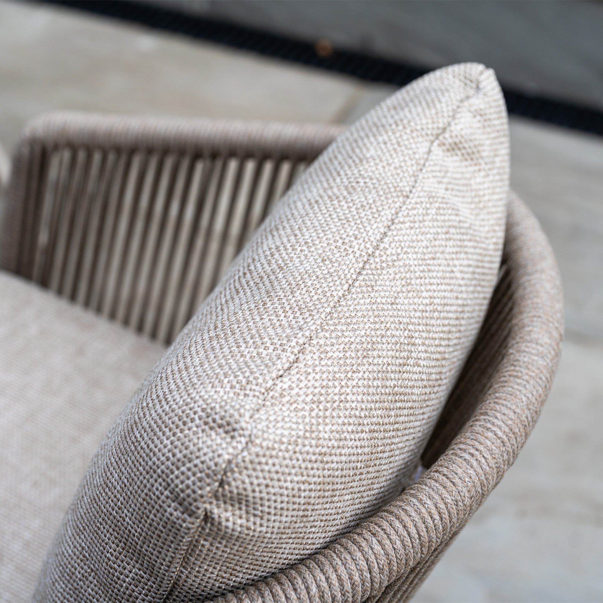 Close-up of a beige woven chair with cushion on a stone patio, featured in our Dekota 6 Seat Rope Dining Set with Albatross Extending Table in Fawn—ideal for creating a welcoming outdoor dining space.