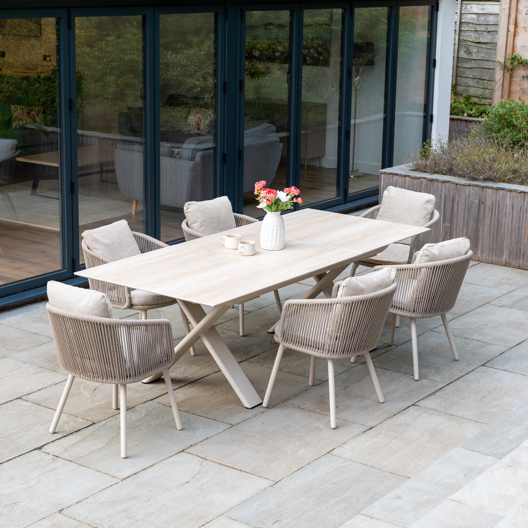 The Dekota 6 Seat Rope Dining Set with Albatross Extending Table in Fawn offers cushioned chairs and elegant style, perfect for outdoor dining and entertaining on any stone patio.