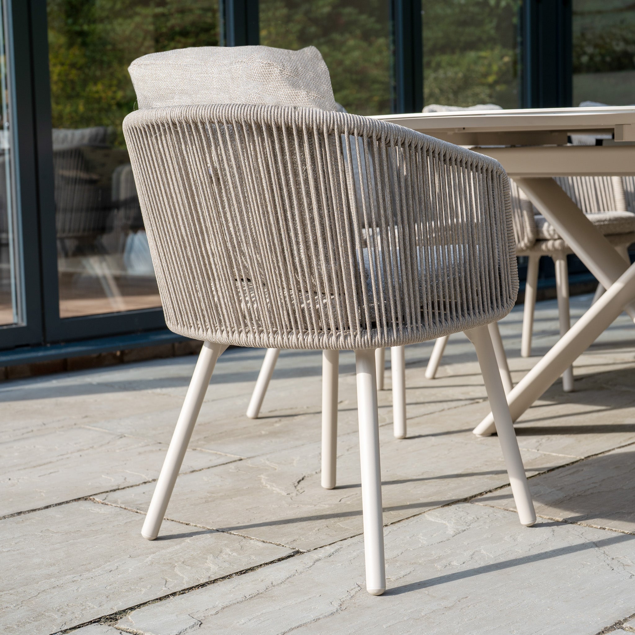The Dekota 8 Seat Oval Rope Dining Set with Albatross Extending Table in Fawn features beige woven chairs with cushions beside a matching table, creating an elegant outdoor dining space perfect for gatherings.