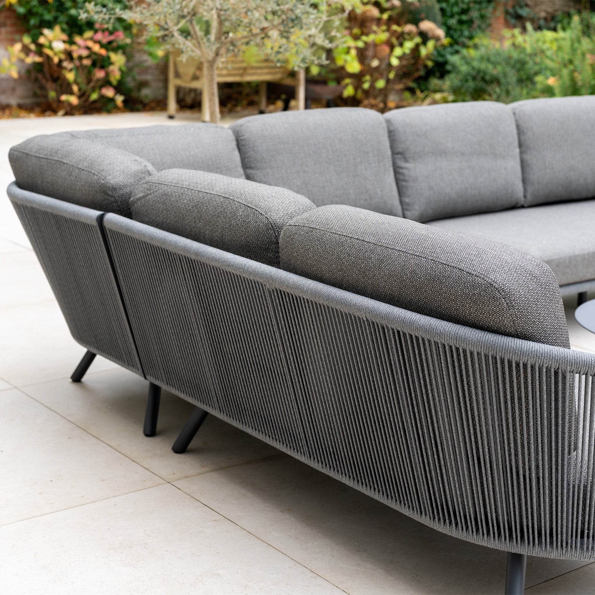 The Dekota Large Corner Sofa Set in Charcoal features a woven back and cushions, making this modern outdoor furniture a stylish choice for any tiled patio.