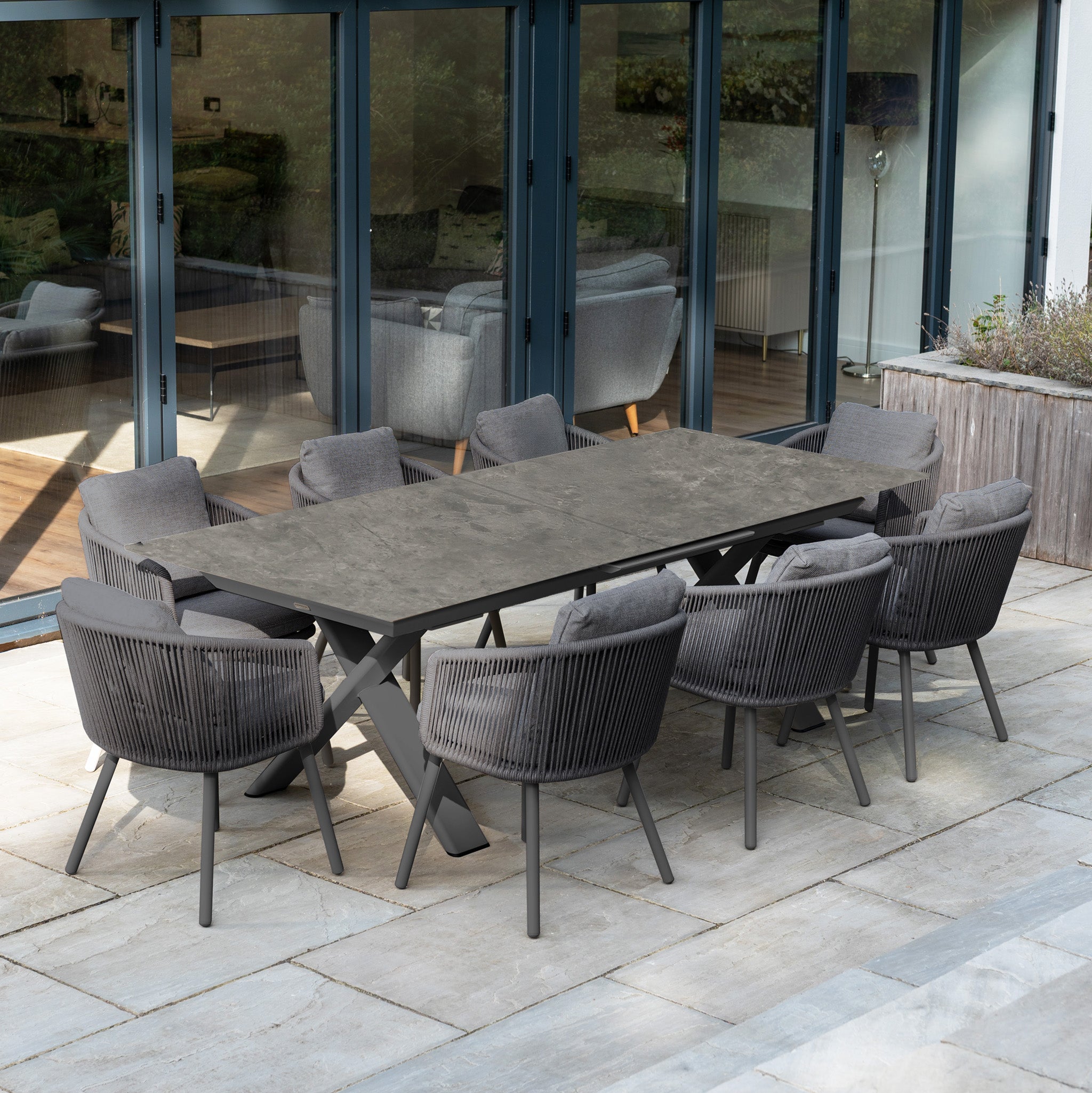 The Dekota 8 Seat Rope Dining Set with Albatross Extending Table in Charcoal features gray cushioned chairs around a sleek, extendable table, perfect for stylish outdoor dining on any stone patio.