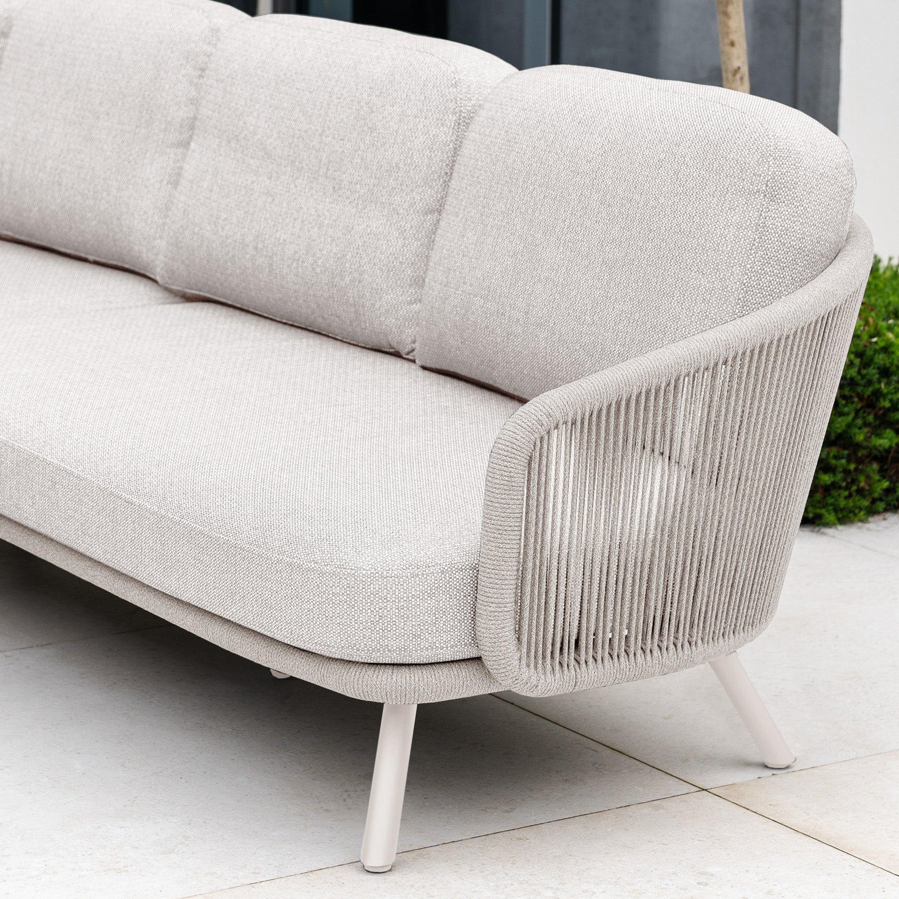 The Dekota Corner Sofa Set in Fawn features rounded cushions and hydrophobic rope weave armrests, making it an ideal outdoor furniture piece for relaxing on your patio.