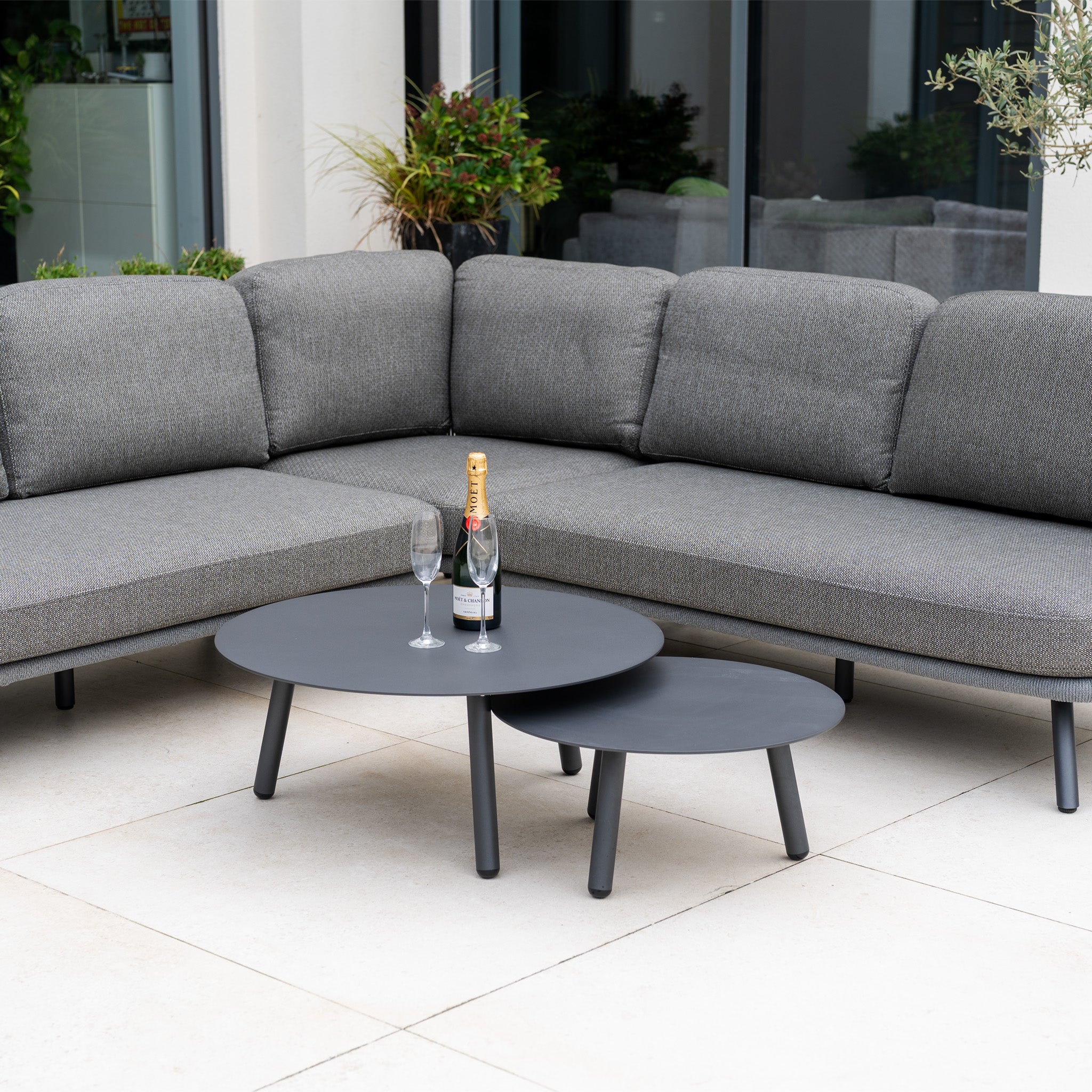 Dekota Corner Sofa Set in Charcoal with hydrophobic rope weave, two round black tables, champagne bottle, and glasses on a patio.