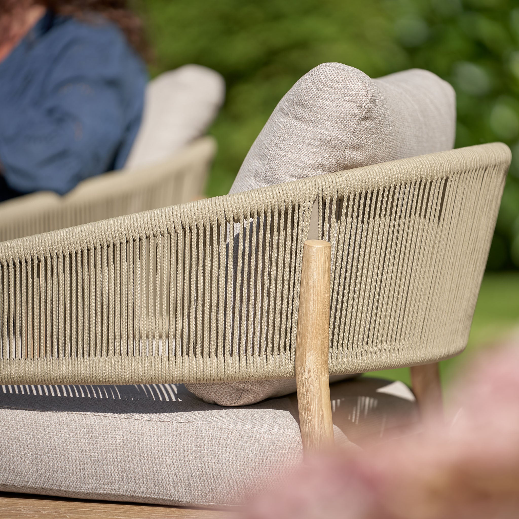 Close-up of a sage green woven patio chair with light cushions in a garden setting, part of the Pacific Lifestyle Denver 2 Seat Sofa Set.