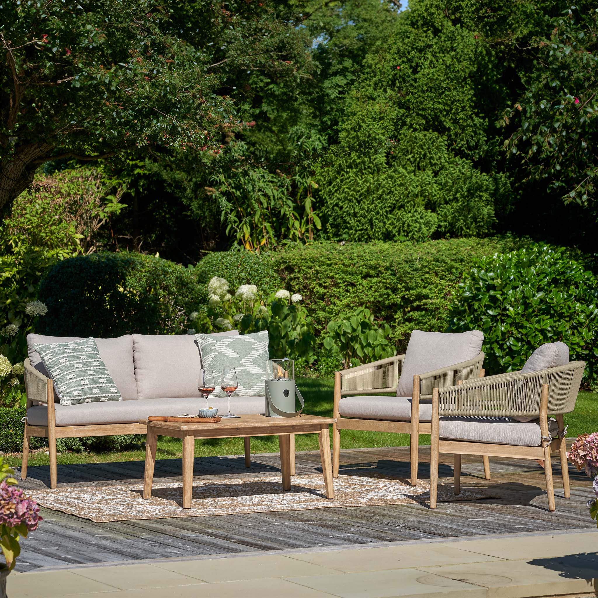 Enhance your outdoor space with the Pacific Lifestyle - Denver 2 Seat Sofa Set in Sage Green, featuring two cushioned chairs and a sofa made from acacia wood, paired with a wooden coffee table amidst lush greenery.