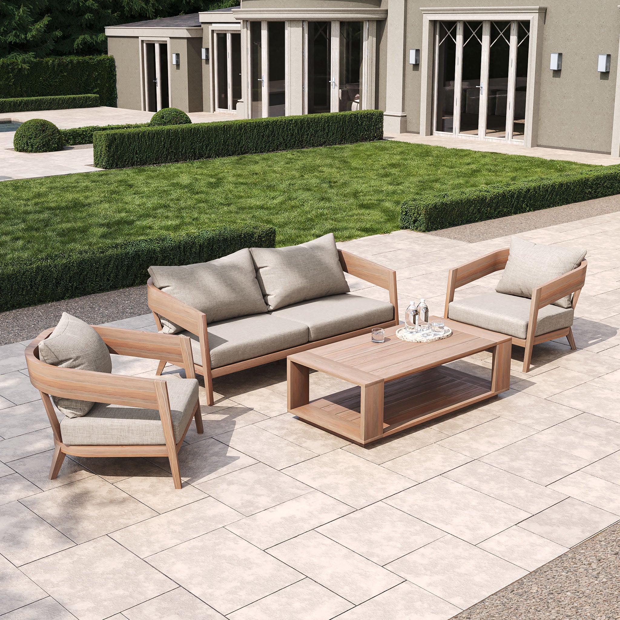 Transform your outdoor area with the Enna 3 Seat Sofa Set in Fawn, including a high-grade teak sofa, matching chairs, and a coffee table on stone tiles.