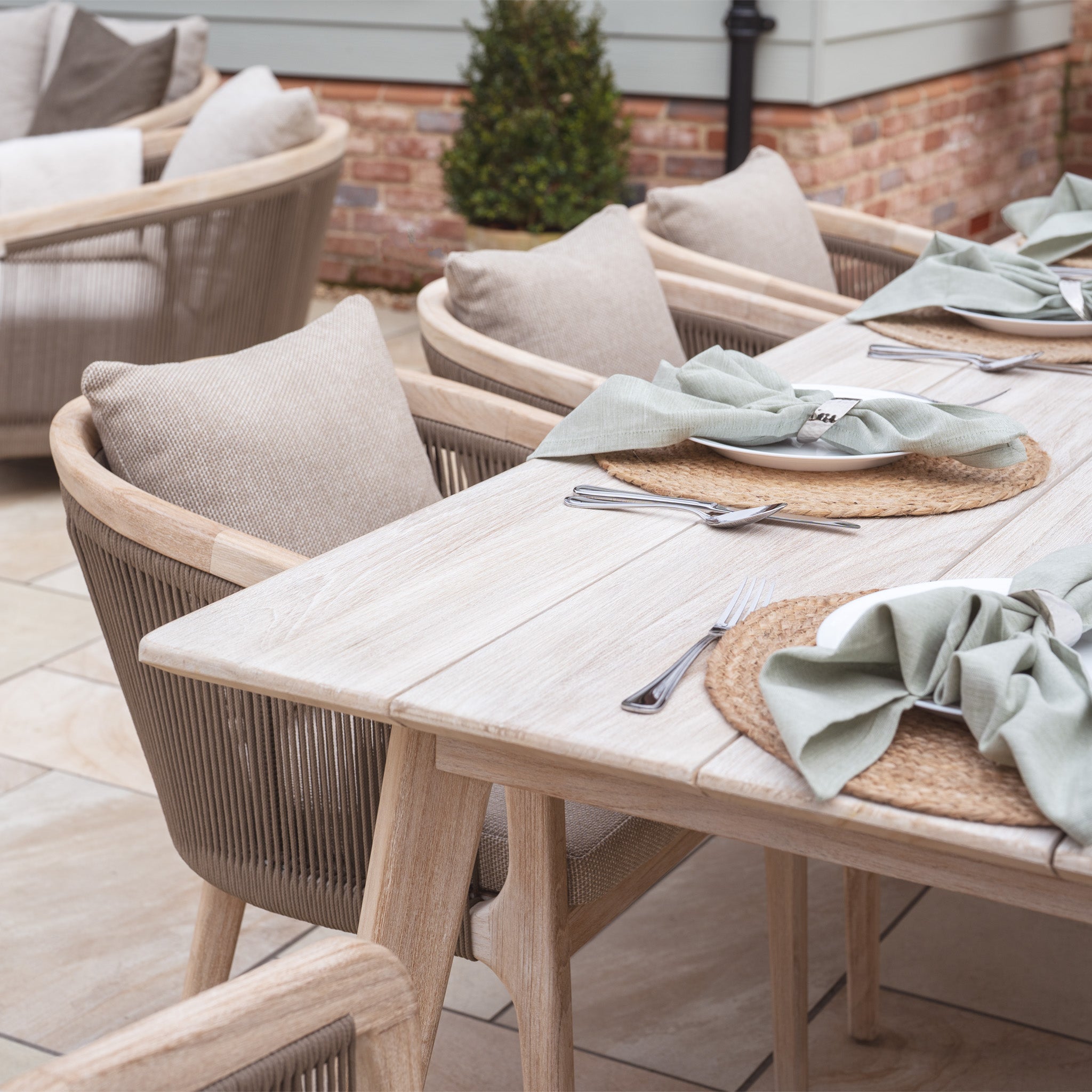 The Evora 8 Seat Rectangular Dining Set in Mocha includes a teak tabletop, wicker chairs, woven placemats, and elegantly folded napkins, showcasing exquisite mocha rope detailing for an ideal blend of style and comfort.