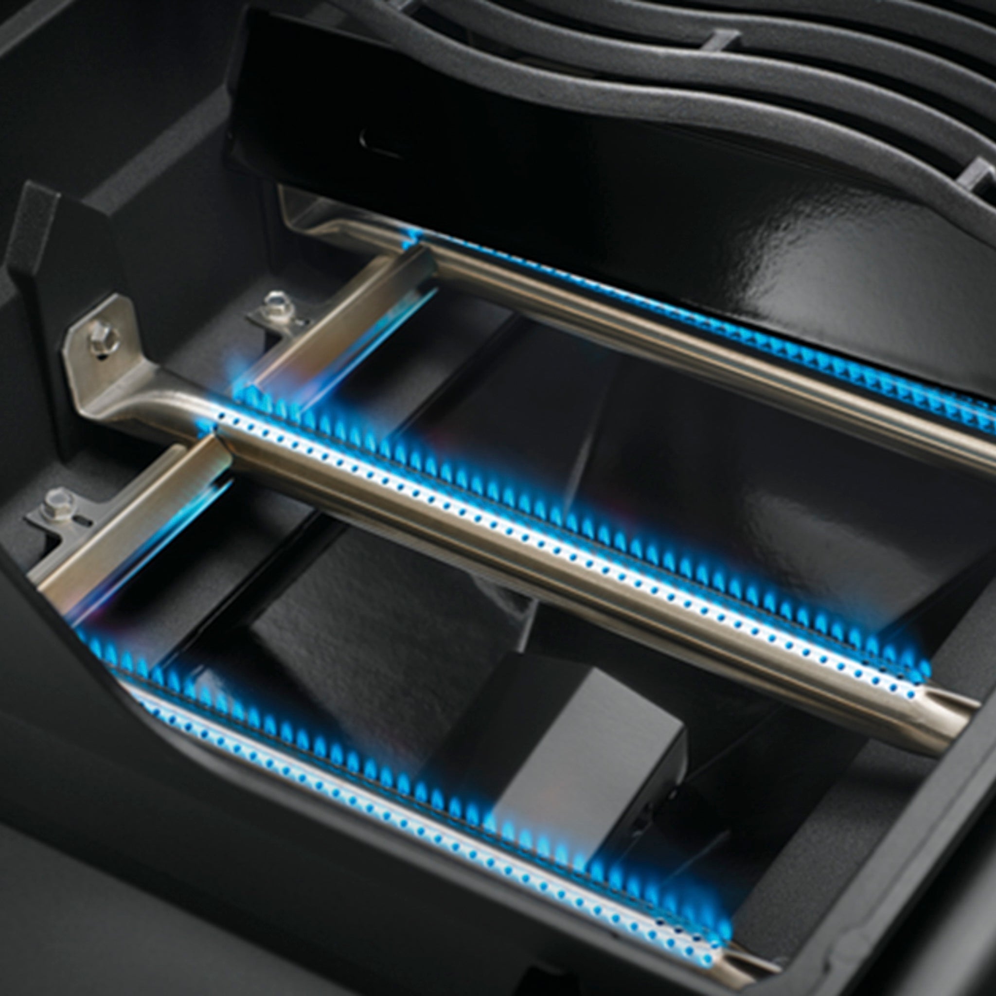 Close-up of a gas grill burner with two lit blue flames in a rectangular metal frame, showcasing the efficiency of the JETFIRE ignition system on the Napoleon Freestyle 365 Gas Barbecue.