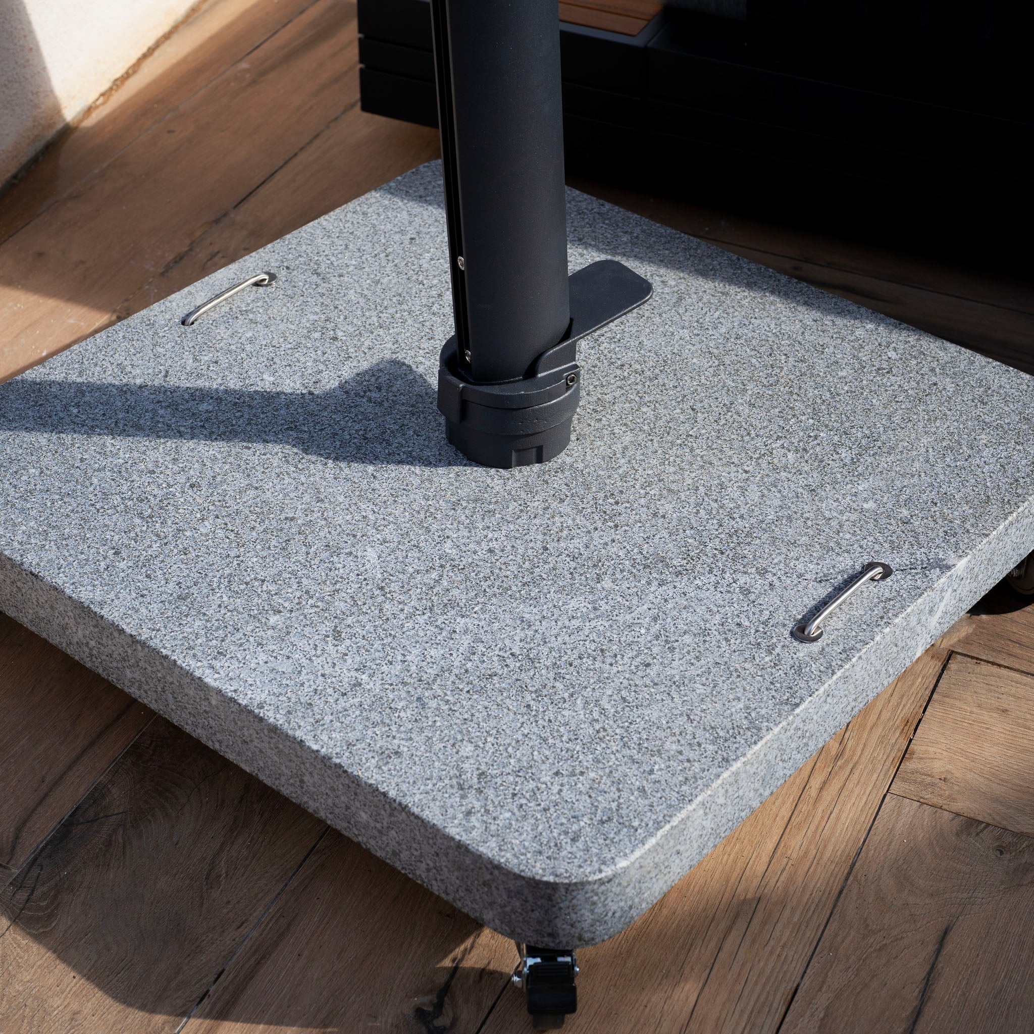 A close-up of the Hacienda 3m x 4m Cantilever Parasol with a charcoal granite base and black pole sits on a wooden deck, offering 360-degree rotation for optimal shade coverage.