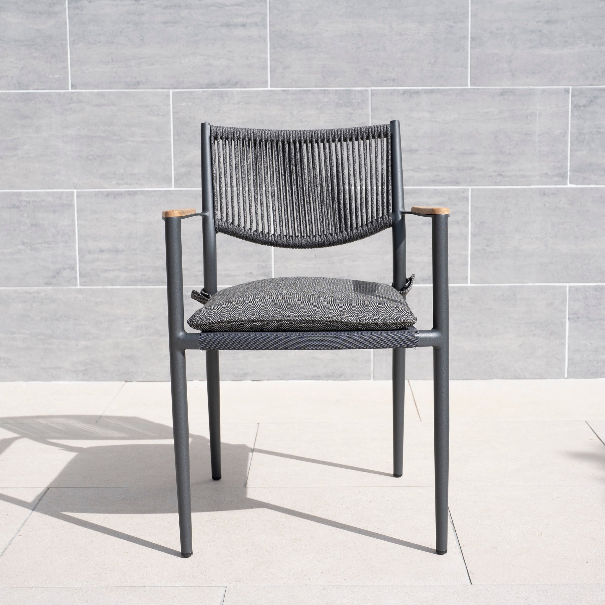 The Tellaro Rope Dining Chair in Grey (6pcs) features a modern design with a weather-resistant cushion, displayed against a light tiled wall and floor.